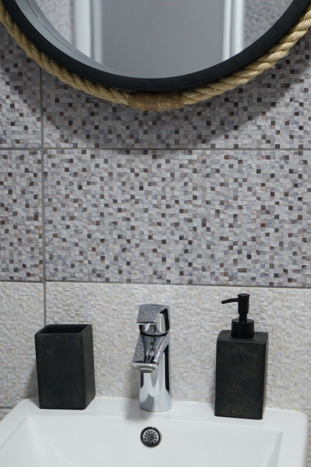 White sink with chrome faucet, black soap dispenser, black tumbler holder