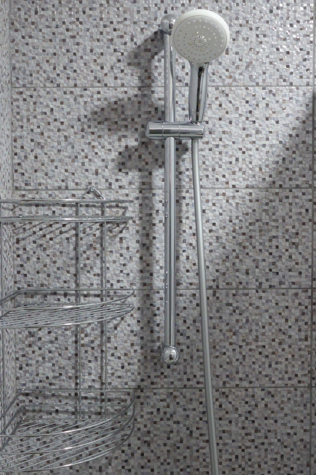 Chrome handheld shower head on sliding rail beside wire corner caddy
