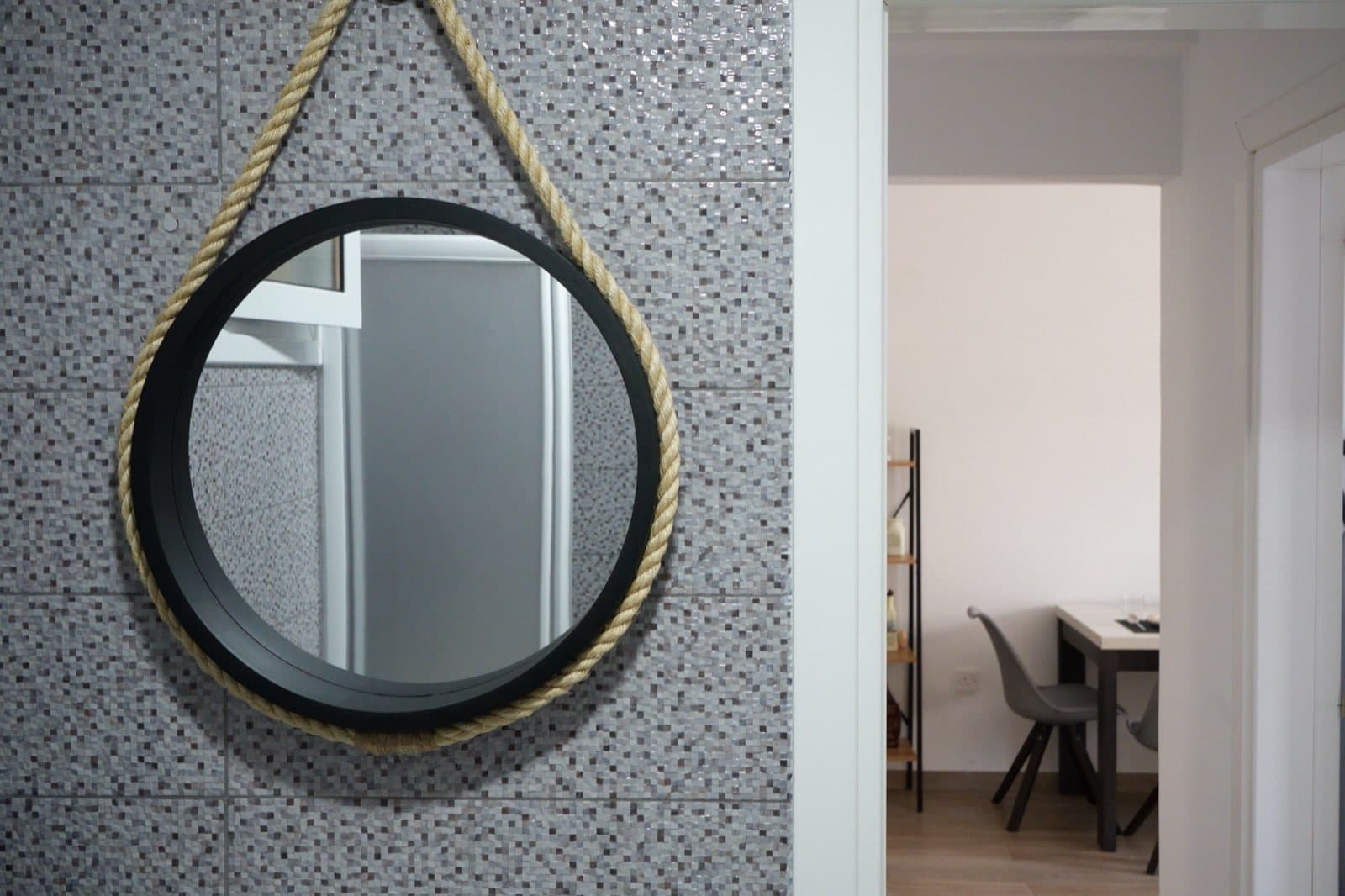 Rope-framed black round mirror on tiled wall above the sink