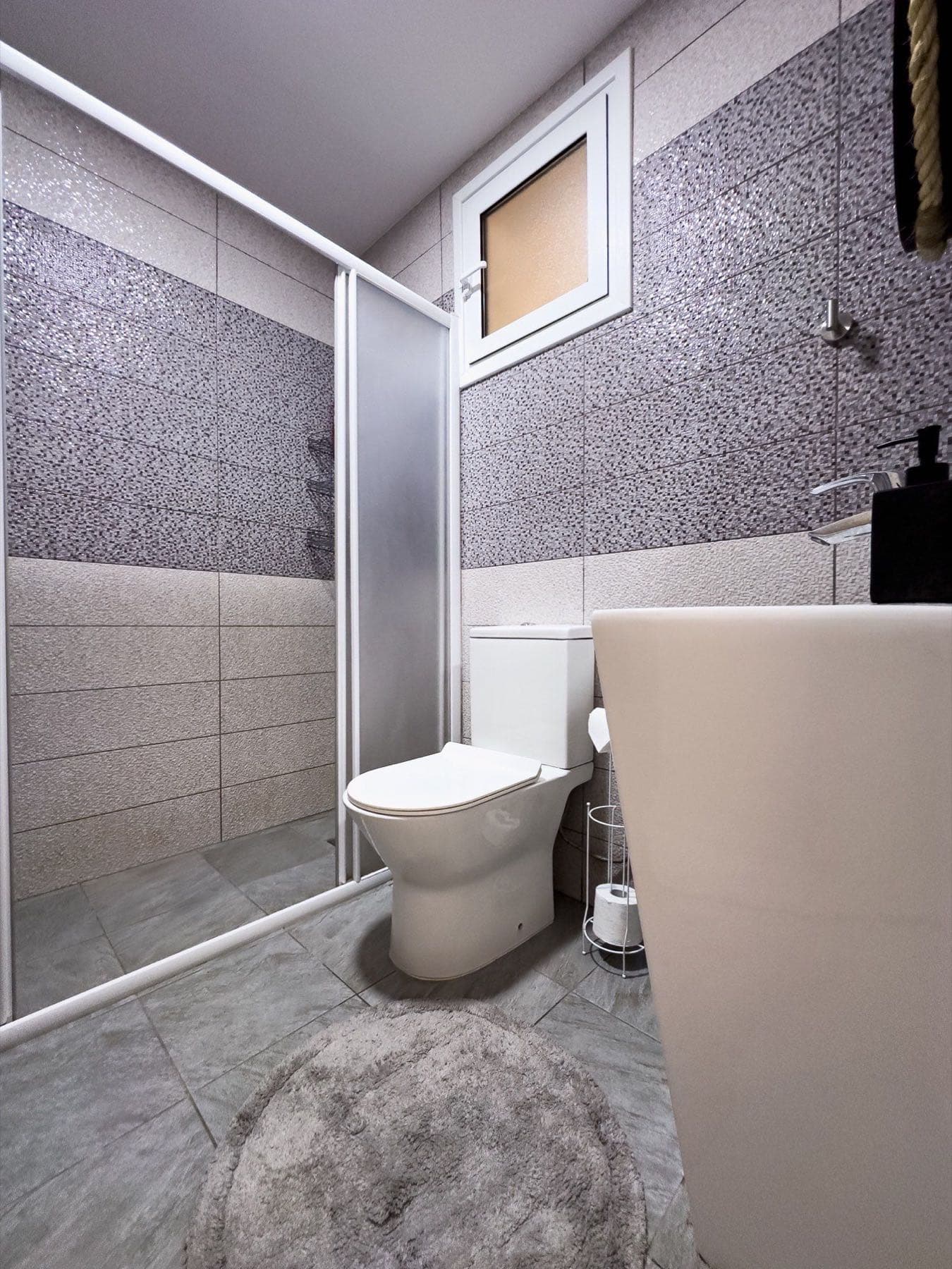 Bathroom with glass shower cabin, white toilet, pedestal sink, and mosaic tile walls