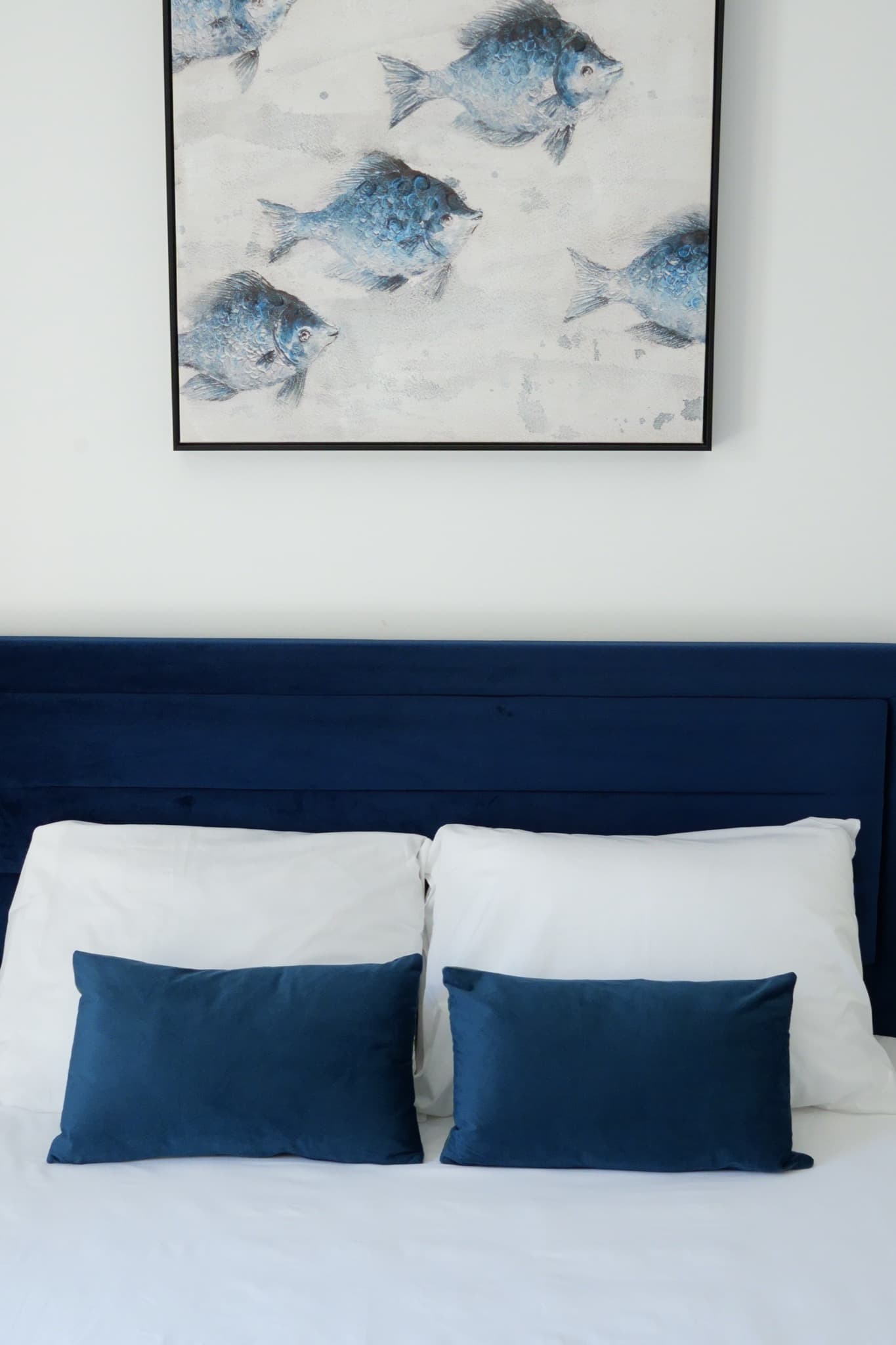 Three blue fish paintings above navy blue upholstered bed headboard