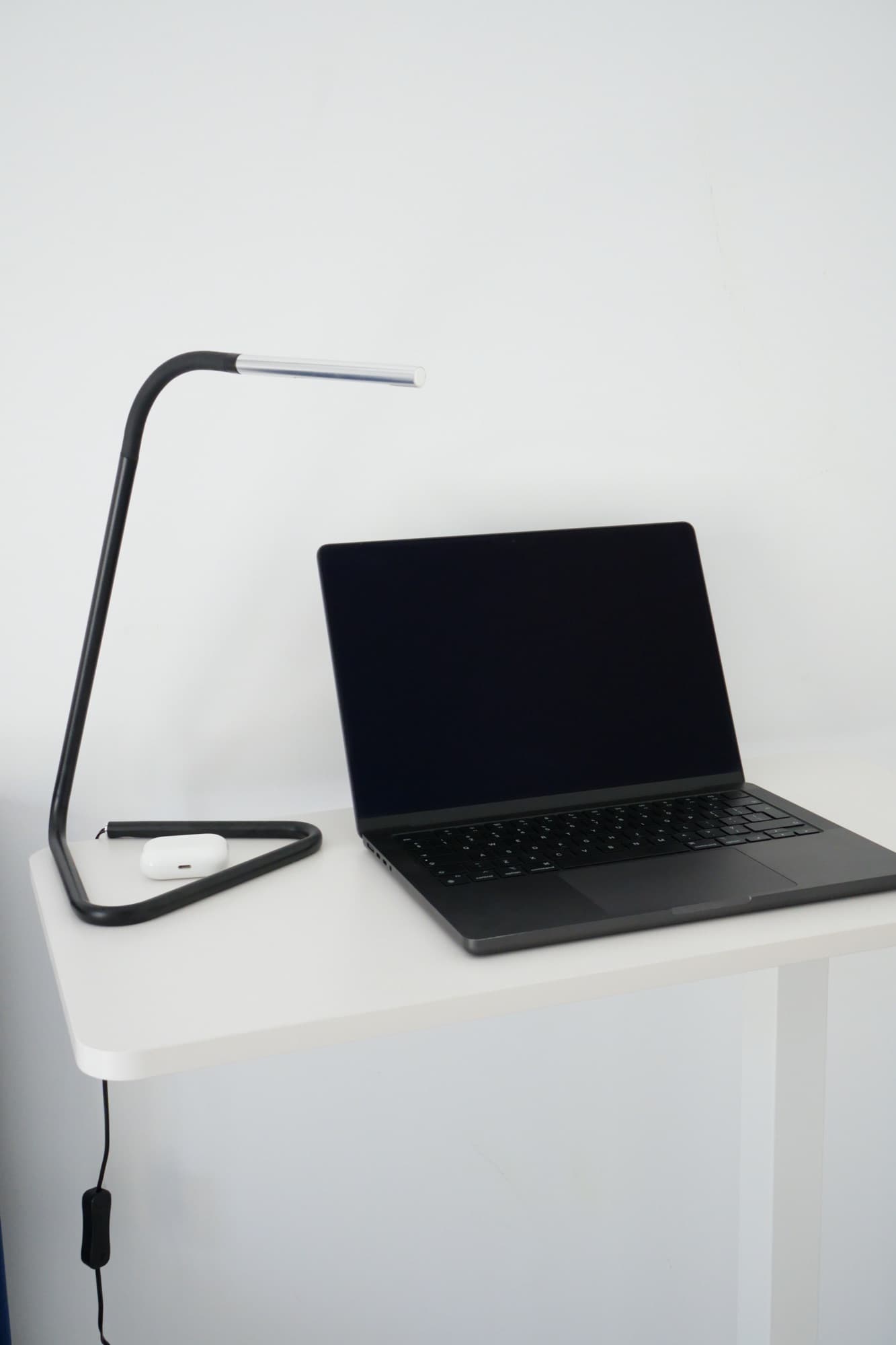 Close-up black laptop keyboard beside desk lamp and white earbud case