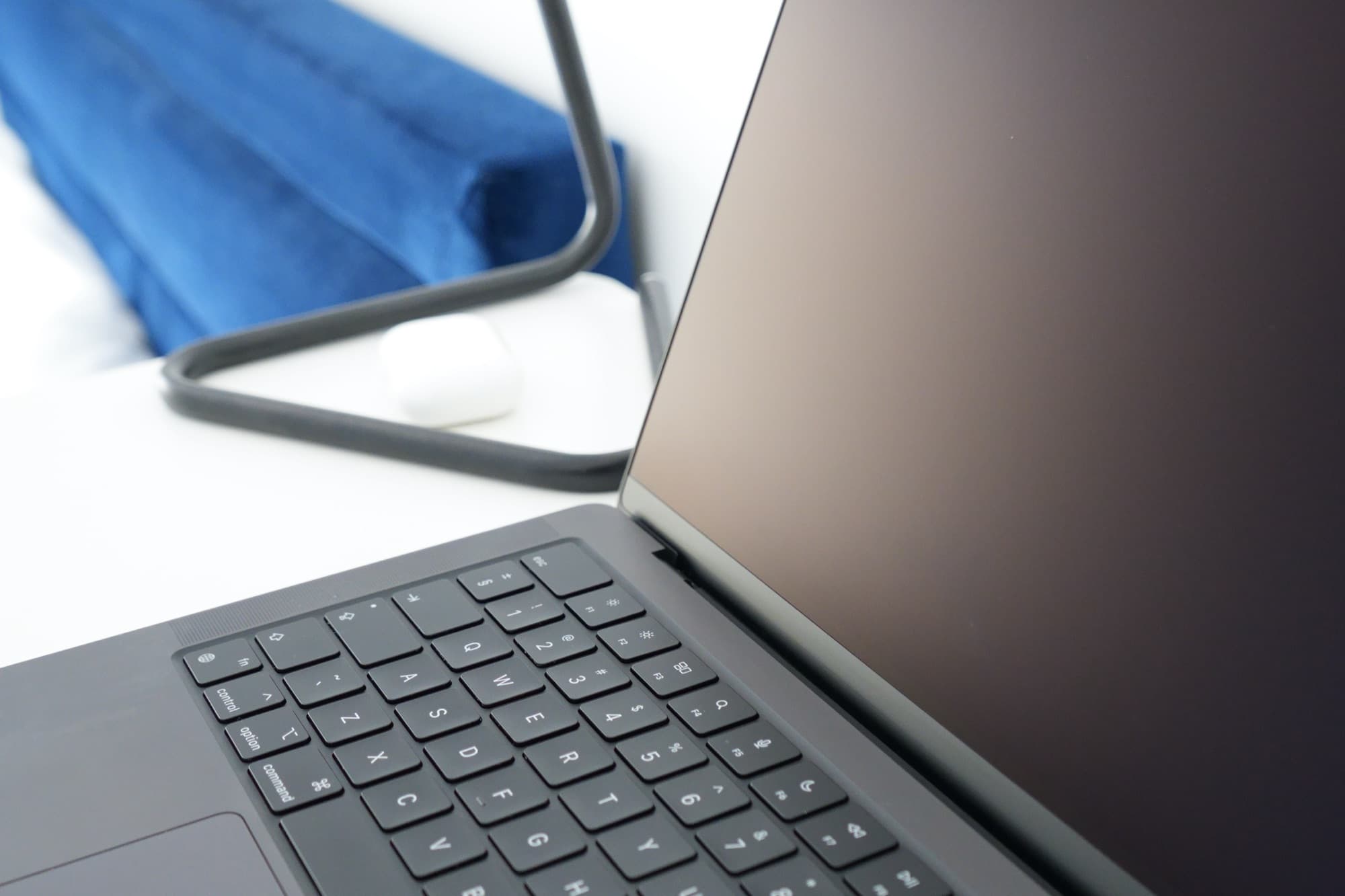 White desk with black laptop, black lamp, and white earbud case