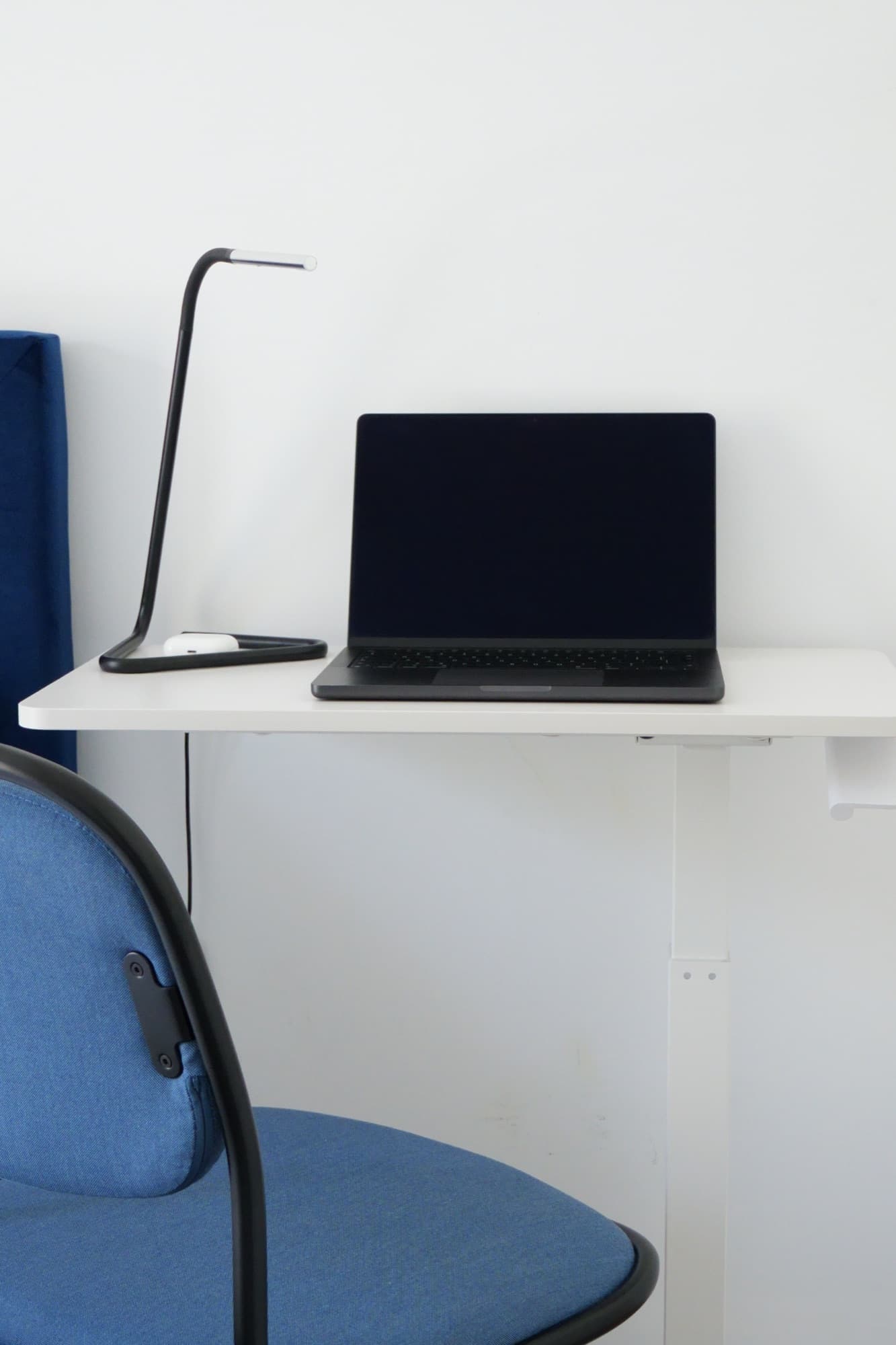 White desk with black laptop, black lamp, and blue chair