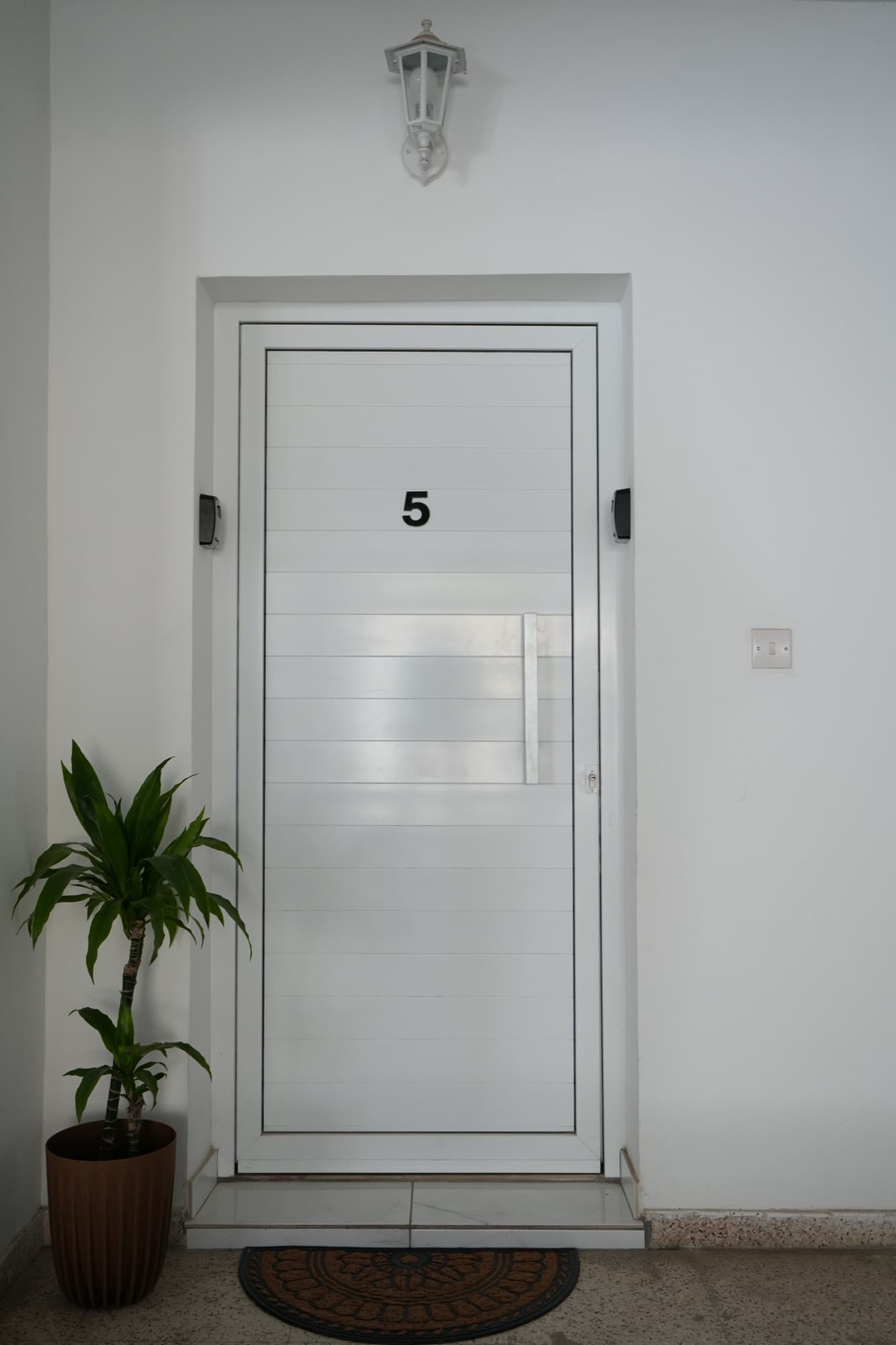 White apartment door number 5 from above with dracaena plant and wall lantern