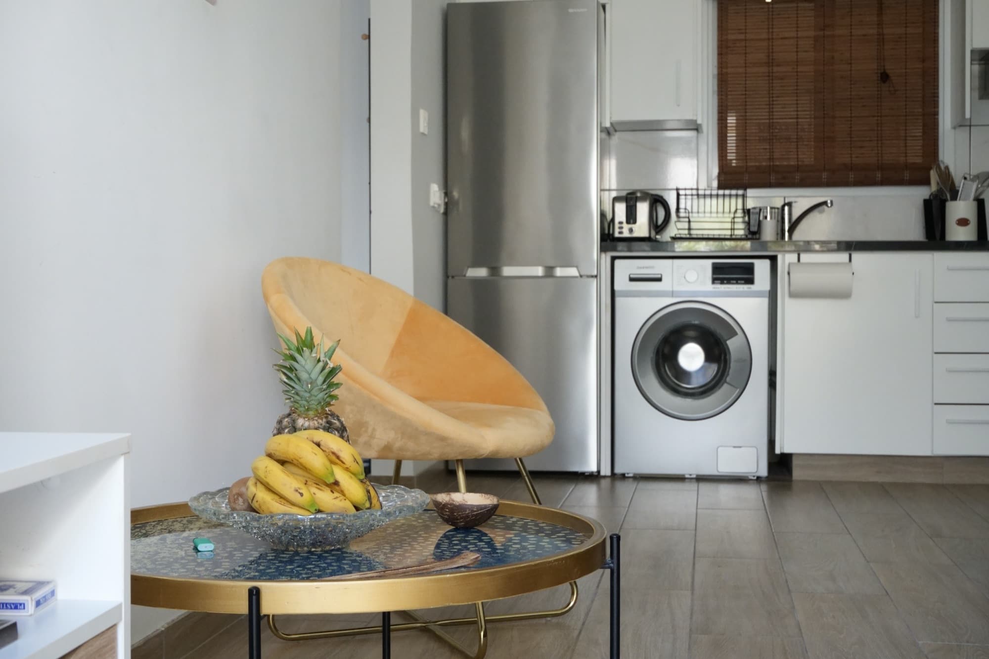 Yellow accent chair facing kitchenette with fridge, washer, and sink