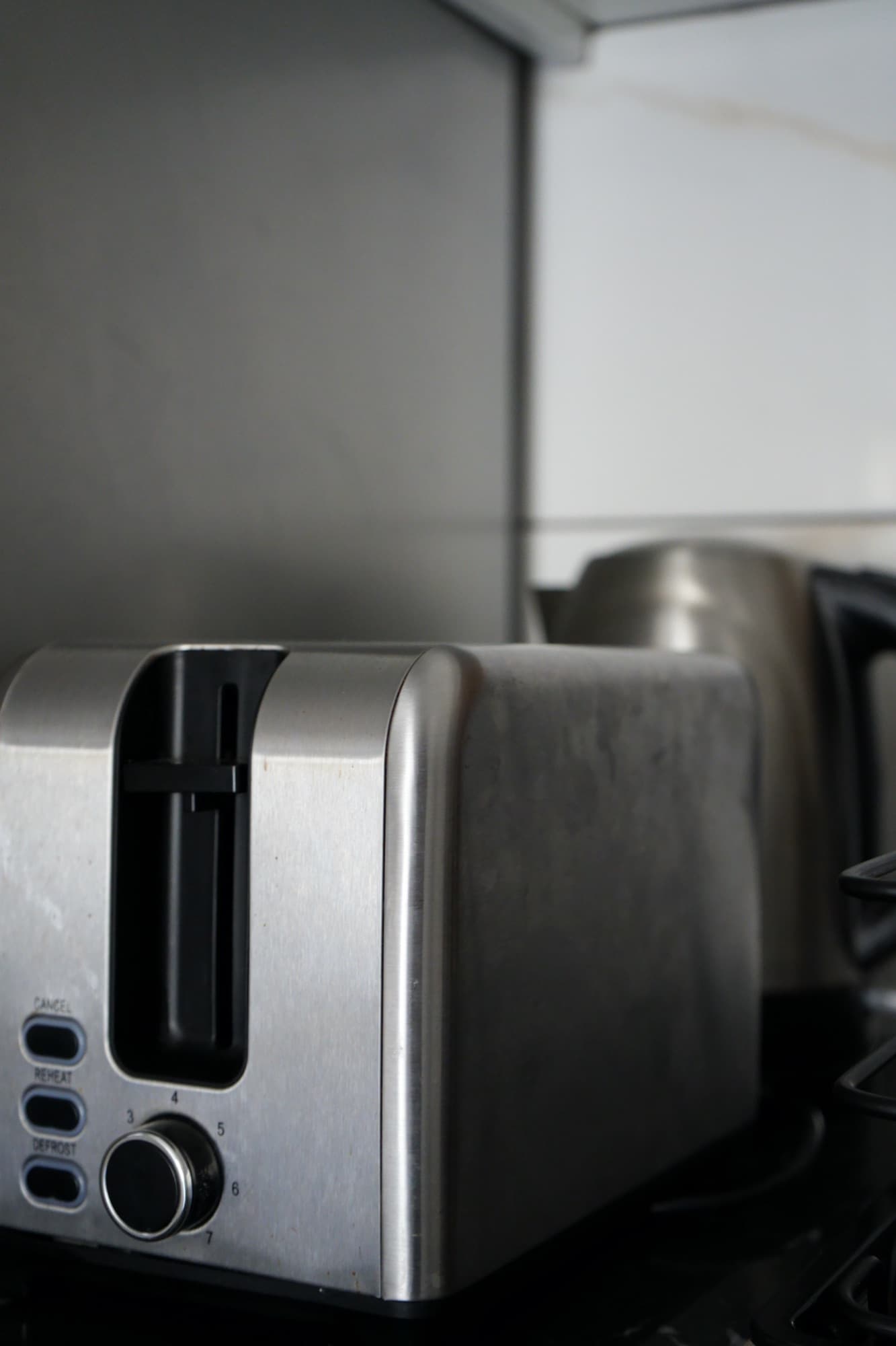 Stainless steel toaster on black countertop beside saucepan and stovetop