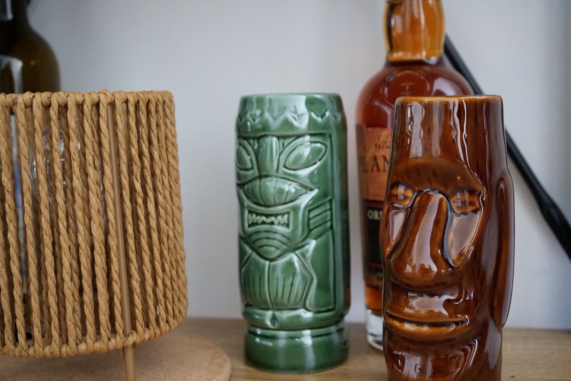 Woven lamp beside green and brown tiki mugs with liquor bottle