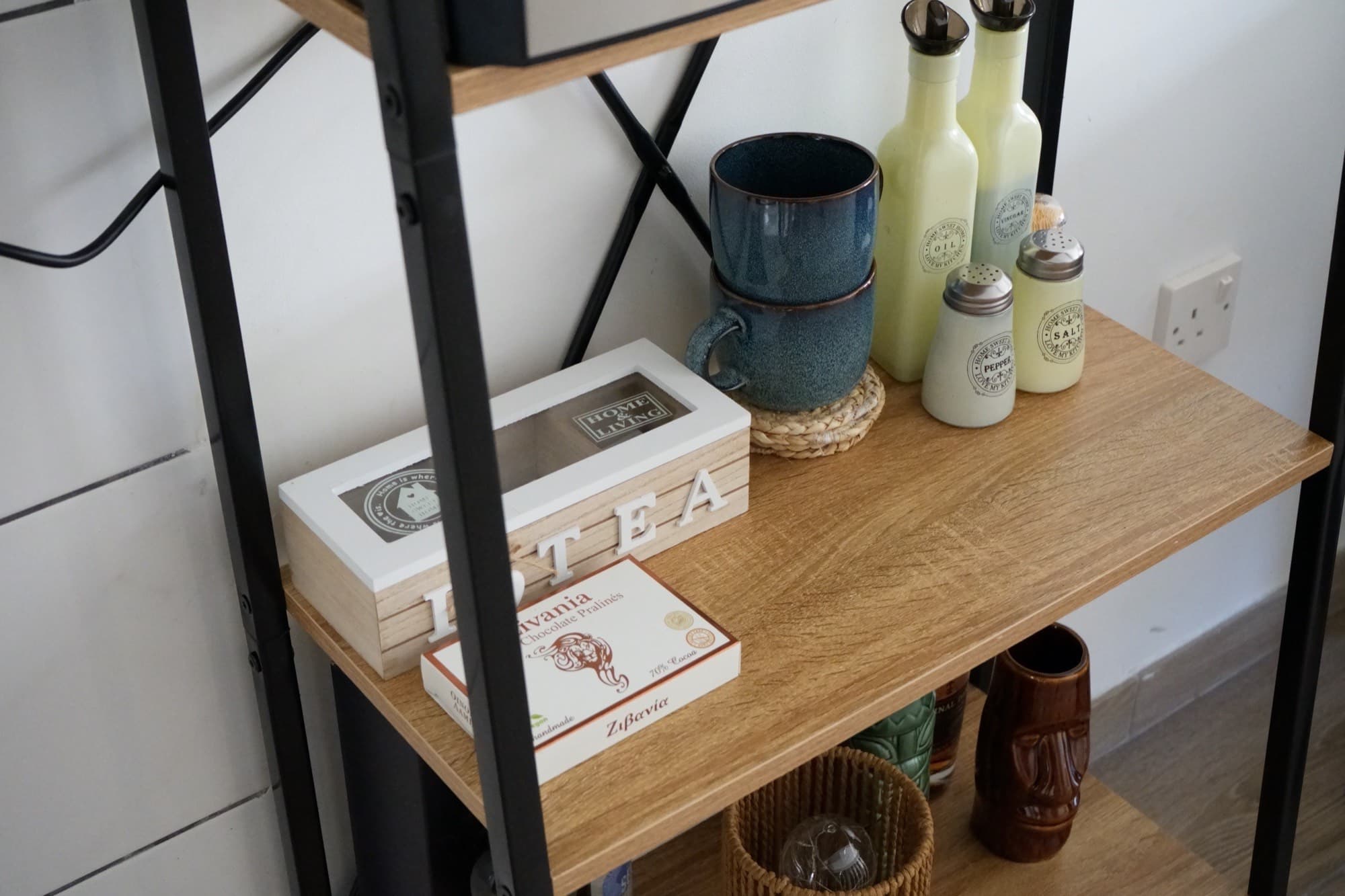 Black metal shelf with tea boxes, ceramic mug, green bottles, and tiki mug