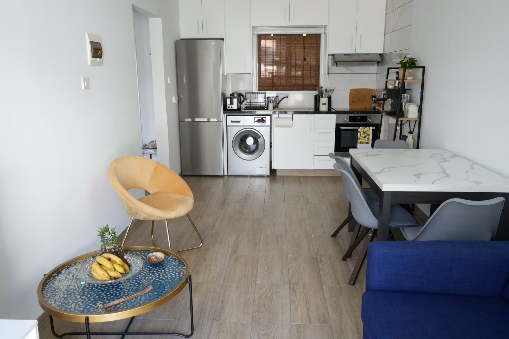 Open-plan kitchen with silver fridge, washing machine, white cabinets, and marble dining table