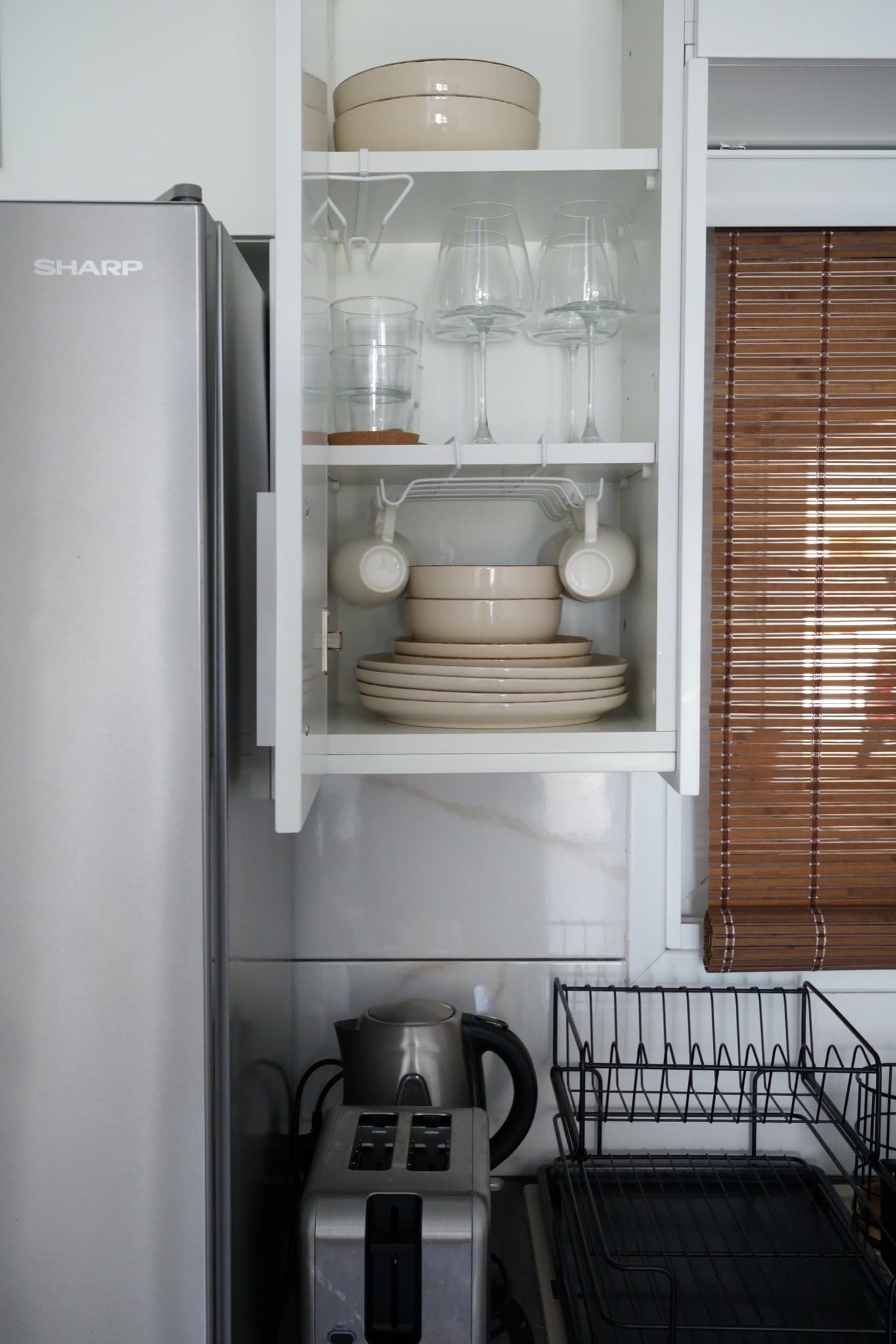 Overhead view of open cabinet with stacked plates, bowls, and glasses beside kettle