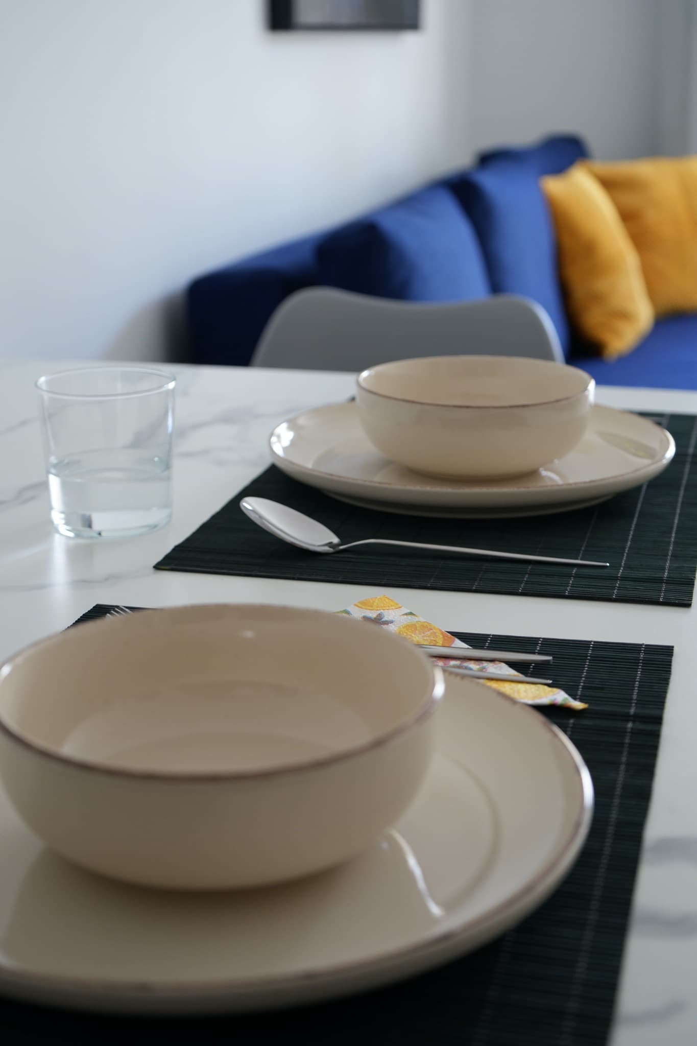 Close-up of beige ceramic plate and bowl on green placemat with glass and cutlery