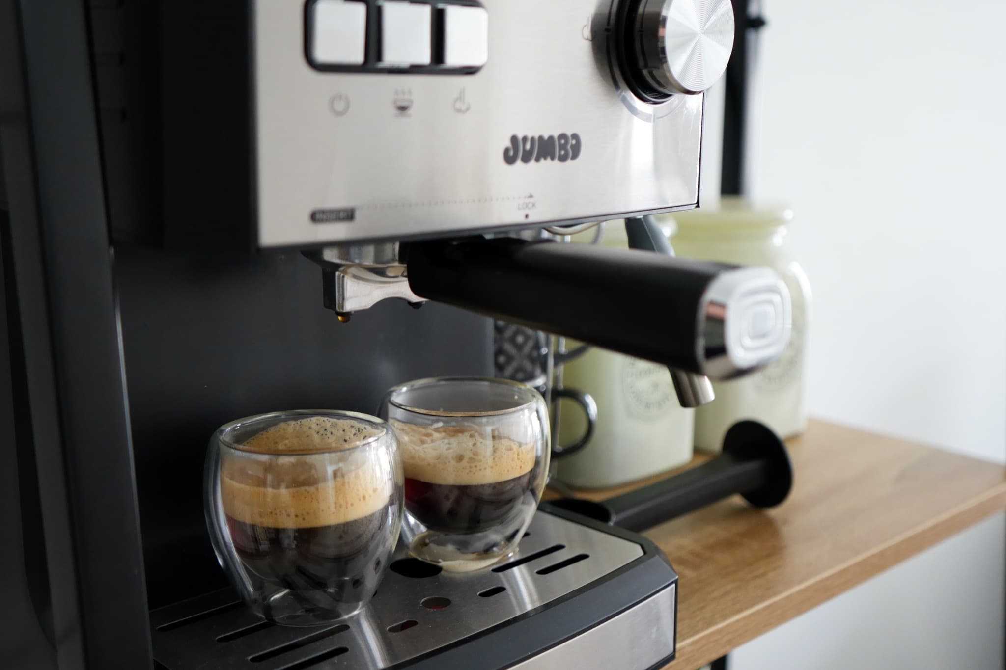 Jumbo espresso machine brewing into two double-walled glass cups on wooden counter
