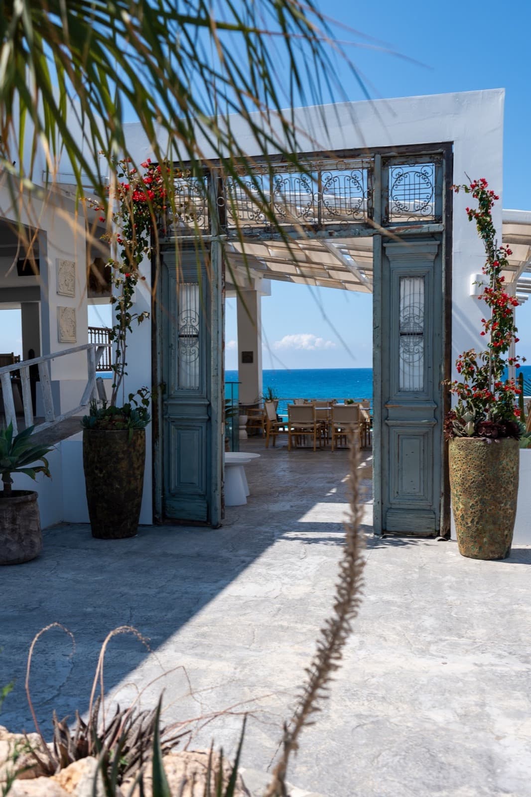 Ornate blue doorway framed by bougainvillea opening onto a sea-view terrace