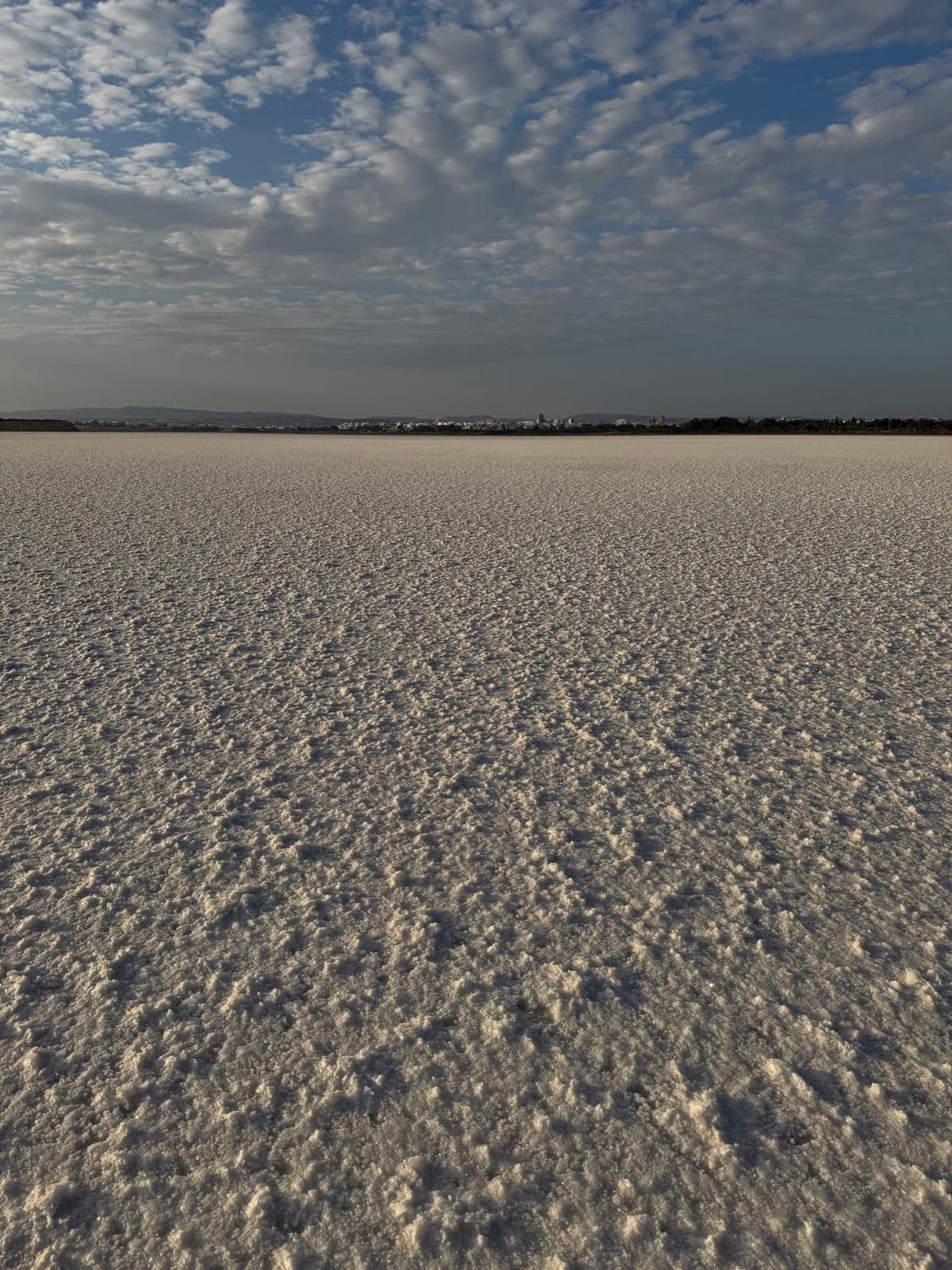 Flat white salt lake surface under cloudy sky with distant city skyline
