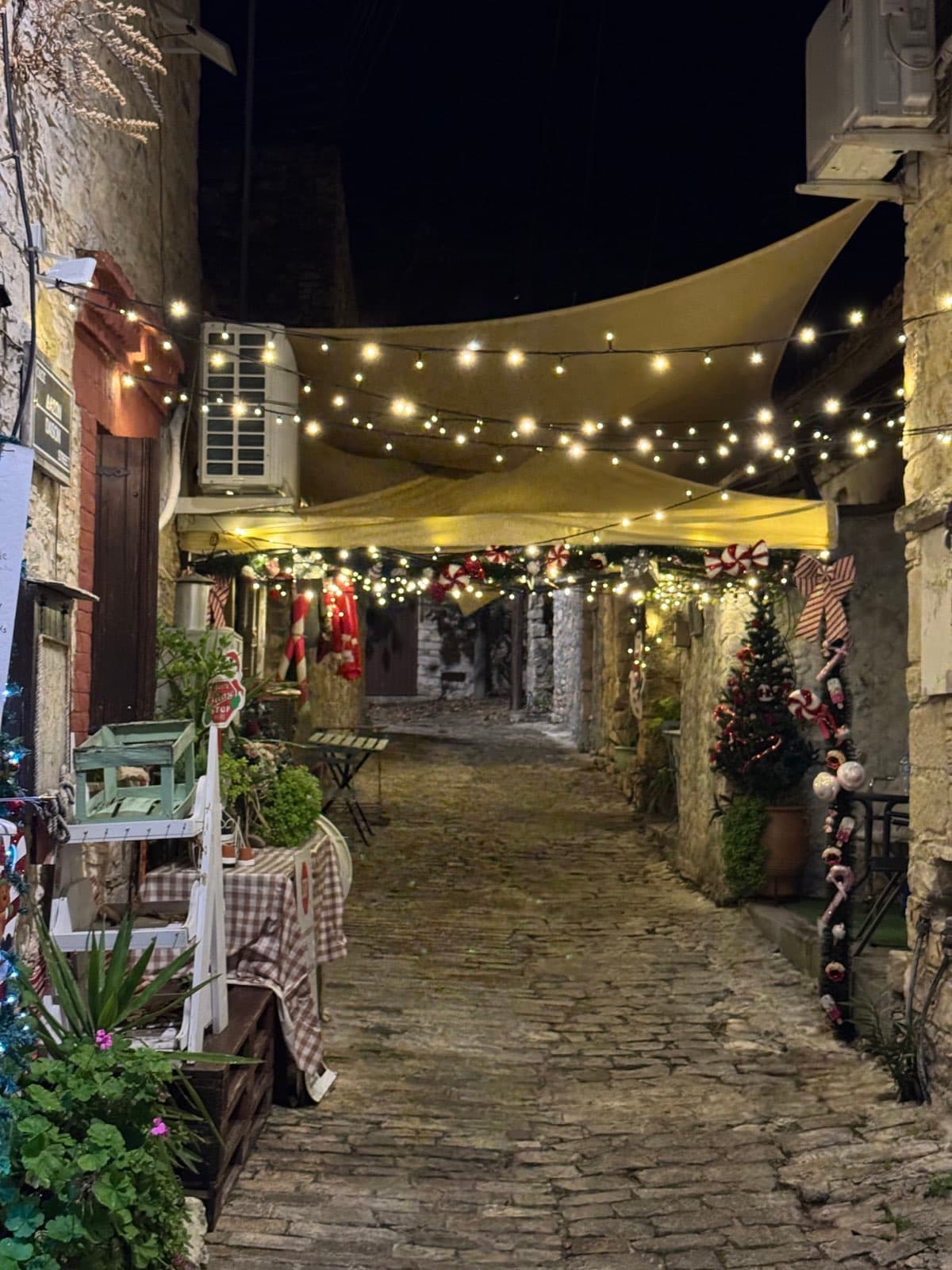 Cobblestone village alley at night with string lights and decorated shop fronts