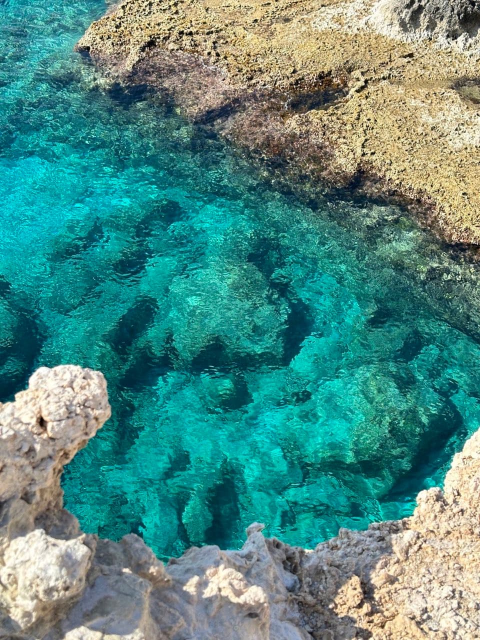 Rocky coastal inlet with turquoise water viewed from limestone cliff edge
