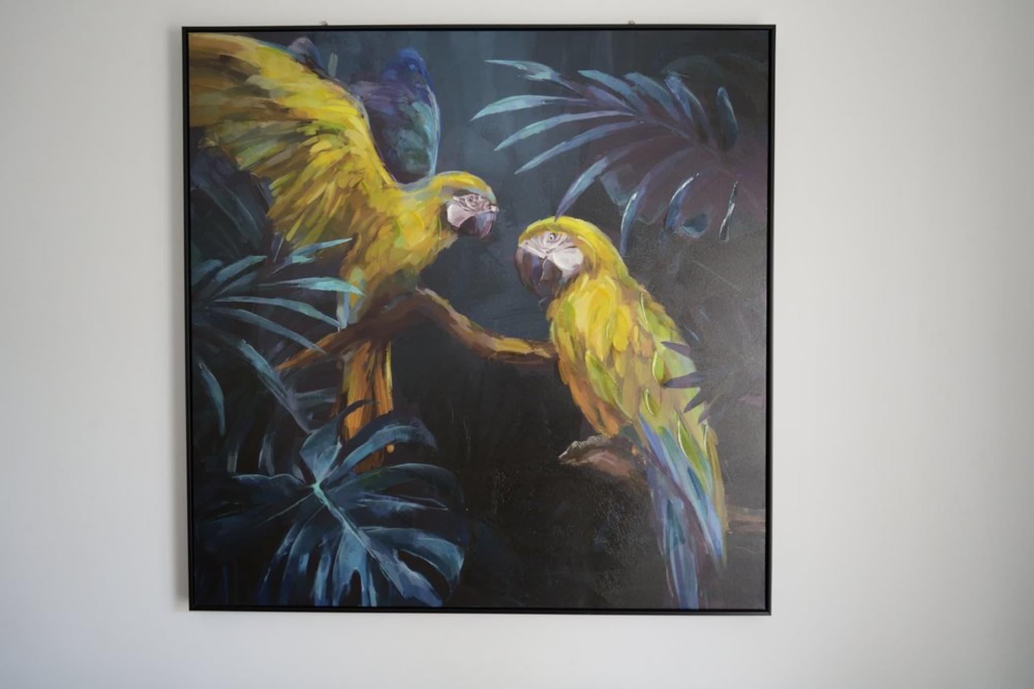 Framed painting of two yellow parrots among dark blue leaves