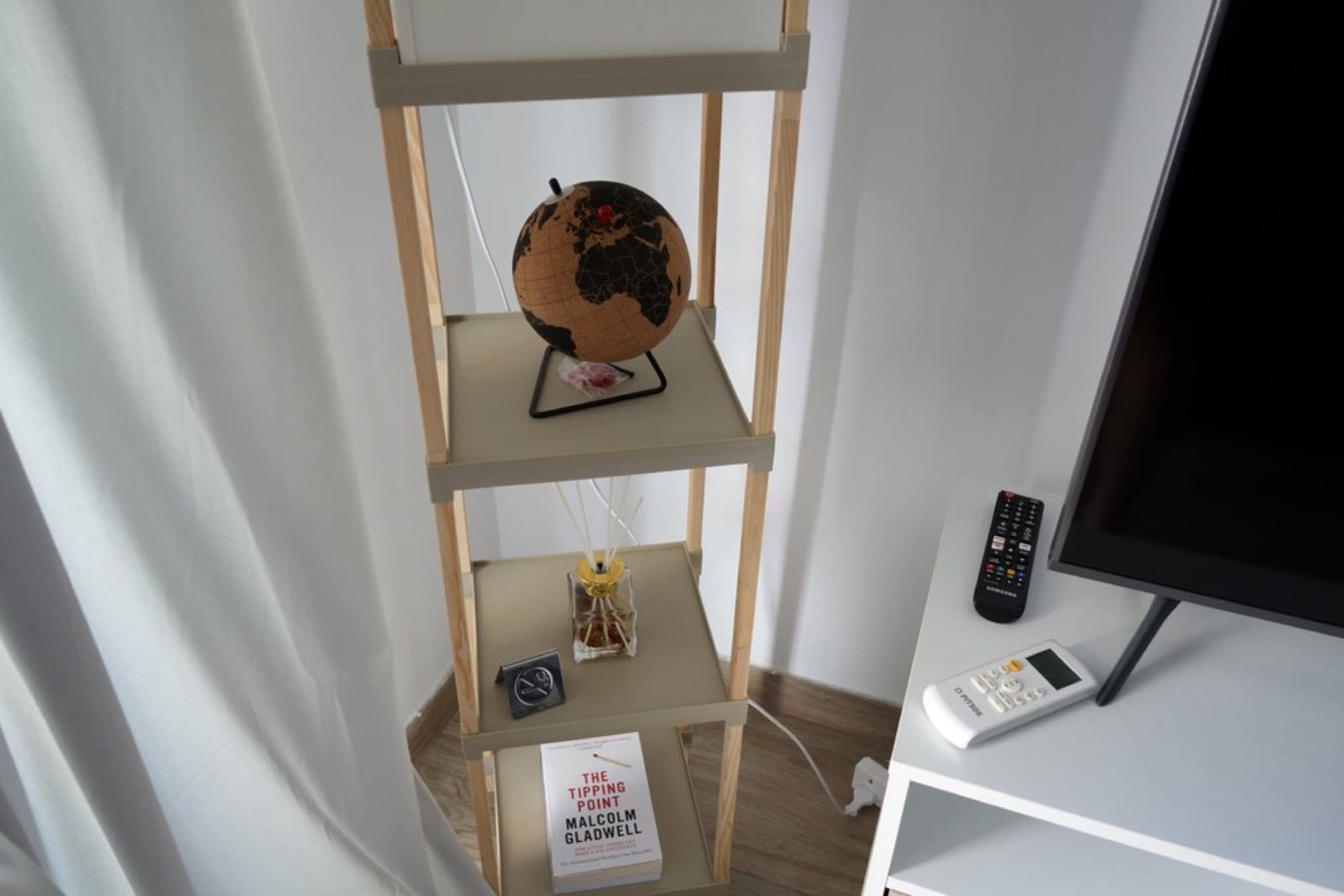 Wooden ladder shelf with cork globe and book beside flat-screen TV and remote