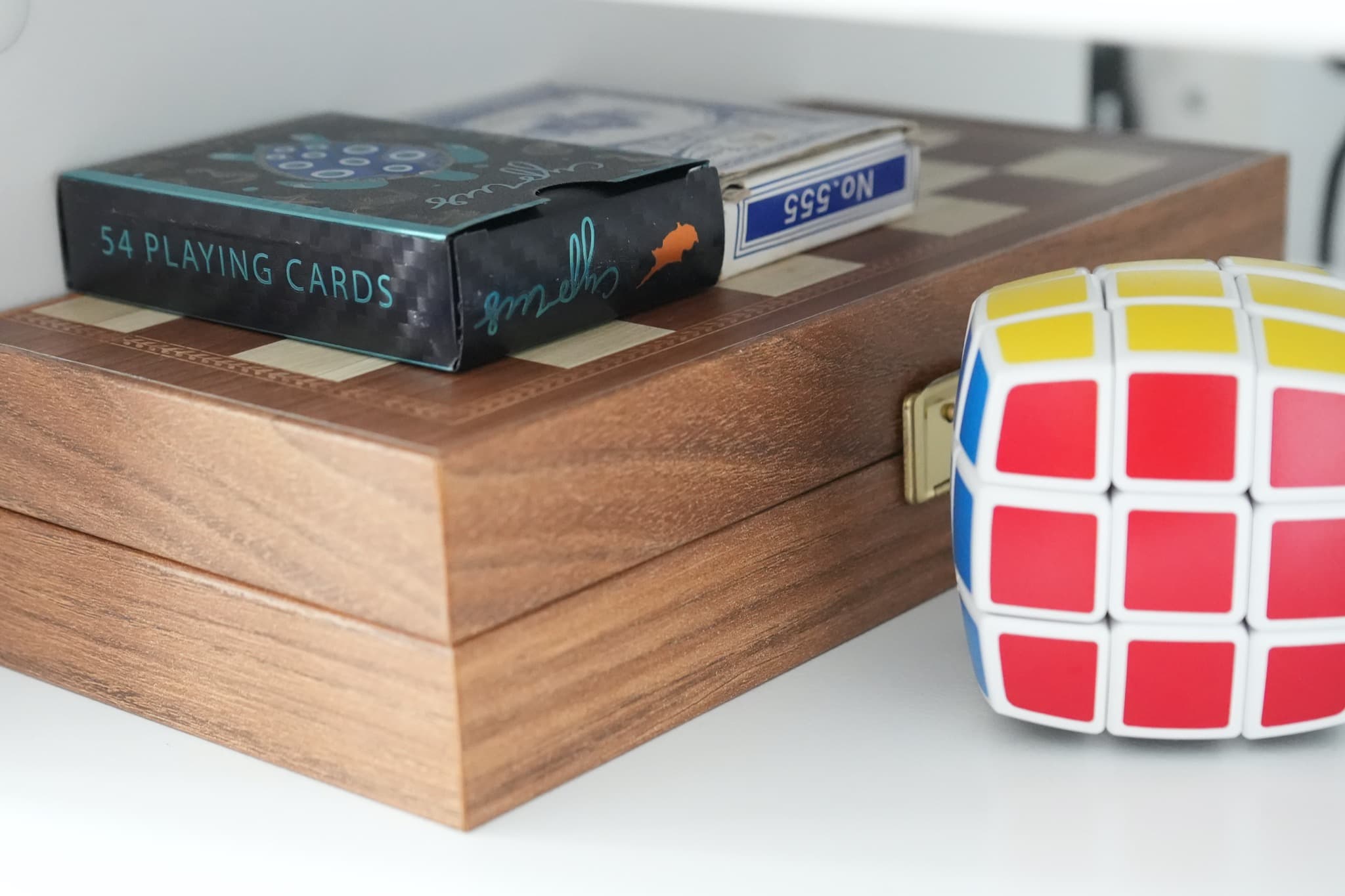 Walnut wooden box with playing cards deck and Rubik's cube on white shelf
