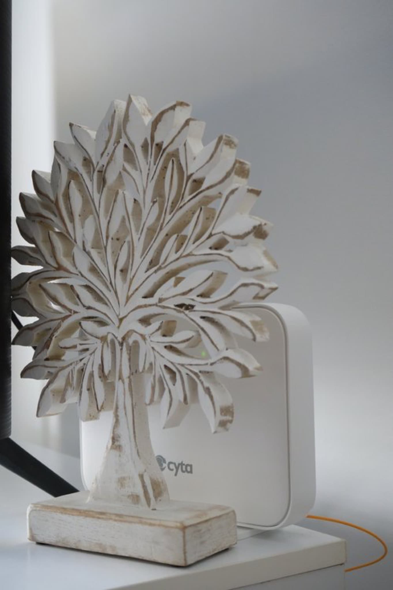 White carved wooden tree sculpture beside Cyta WiFi router on white windowsill