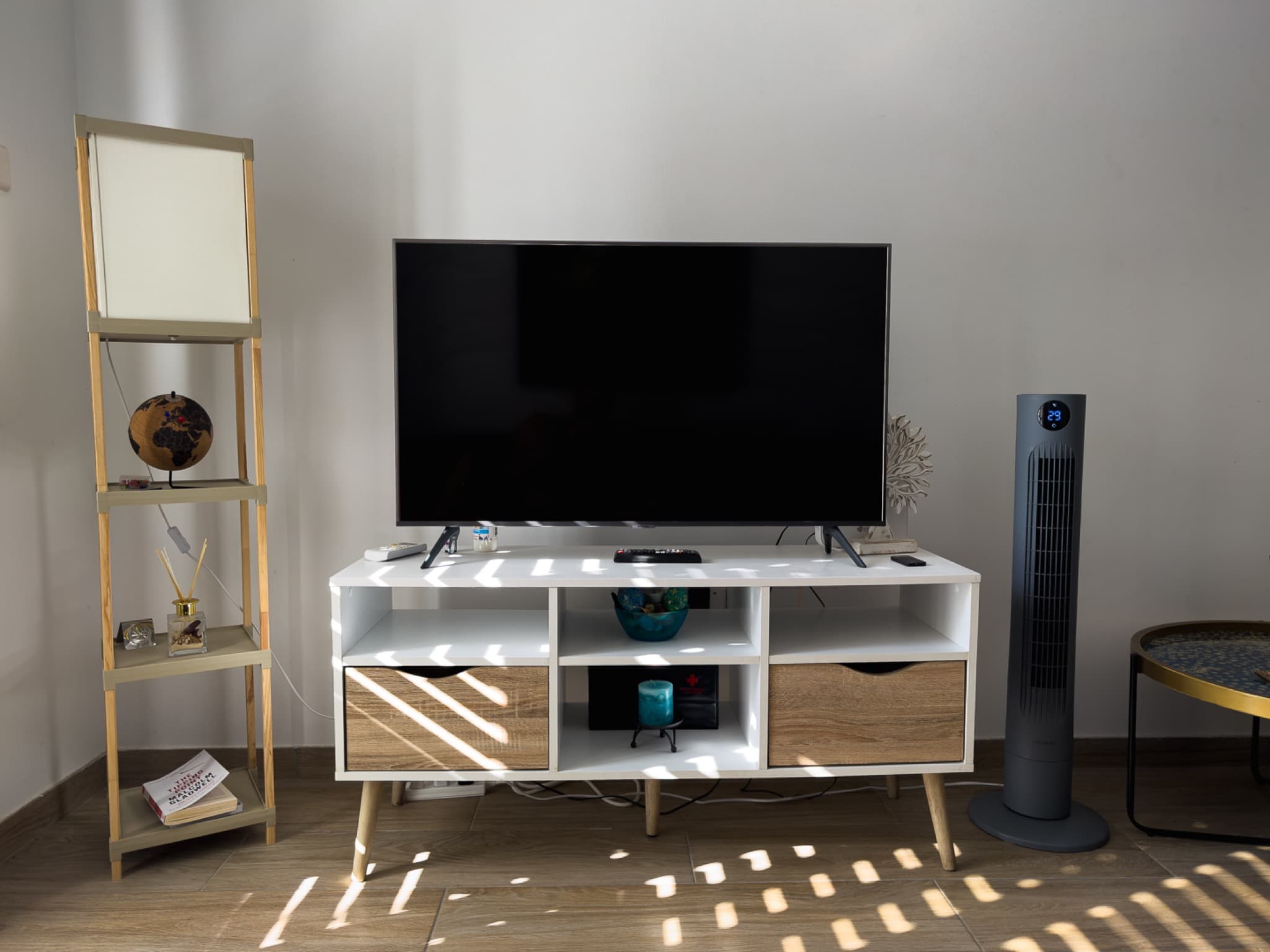 Flat-screen TV on white and oak media unit with ladder shelf and tower fan
