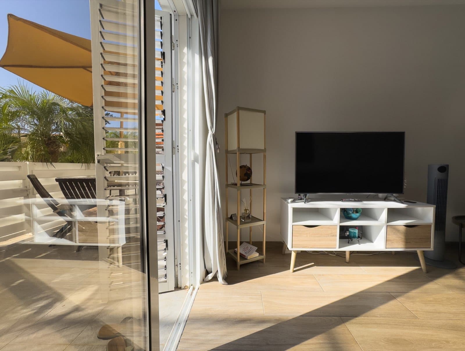 Open sliding glass door to terrace with TV unit and ladder shelf inside