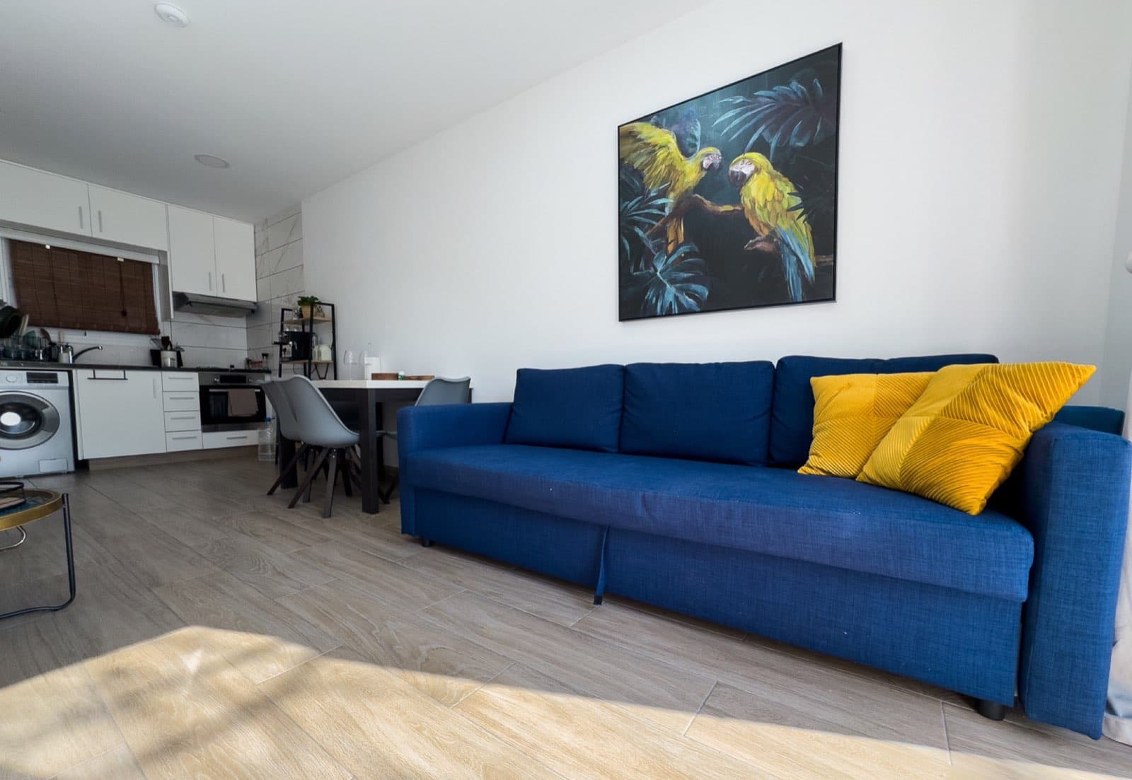Blue sofa with yellow cushions and parrot painting with open-plan kitchen behind