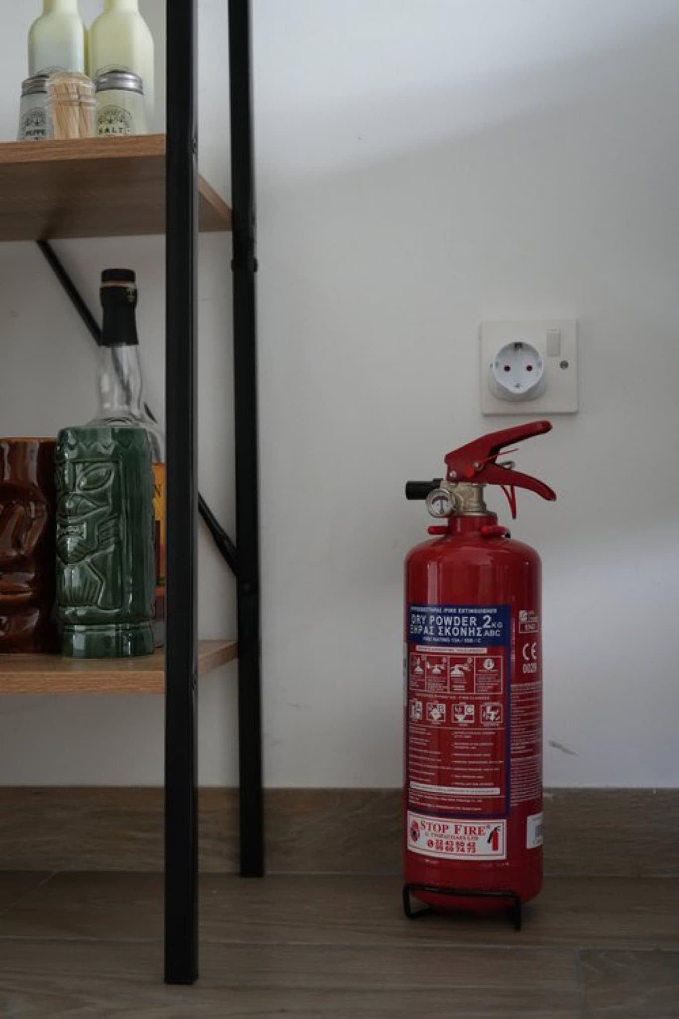 Red 2 kg dry powder fire extinguisher standing on floor beside kitchen shelving