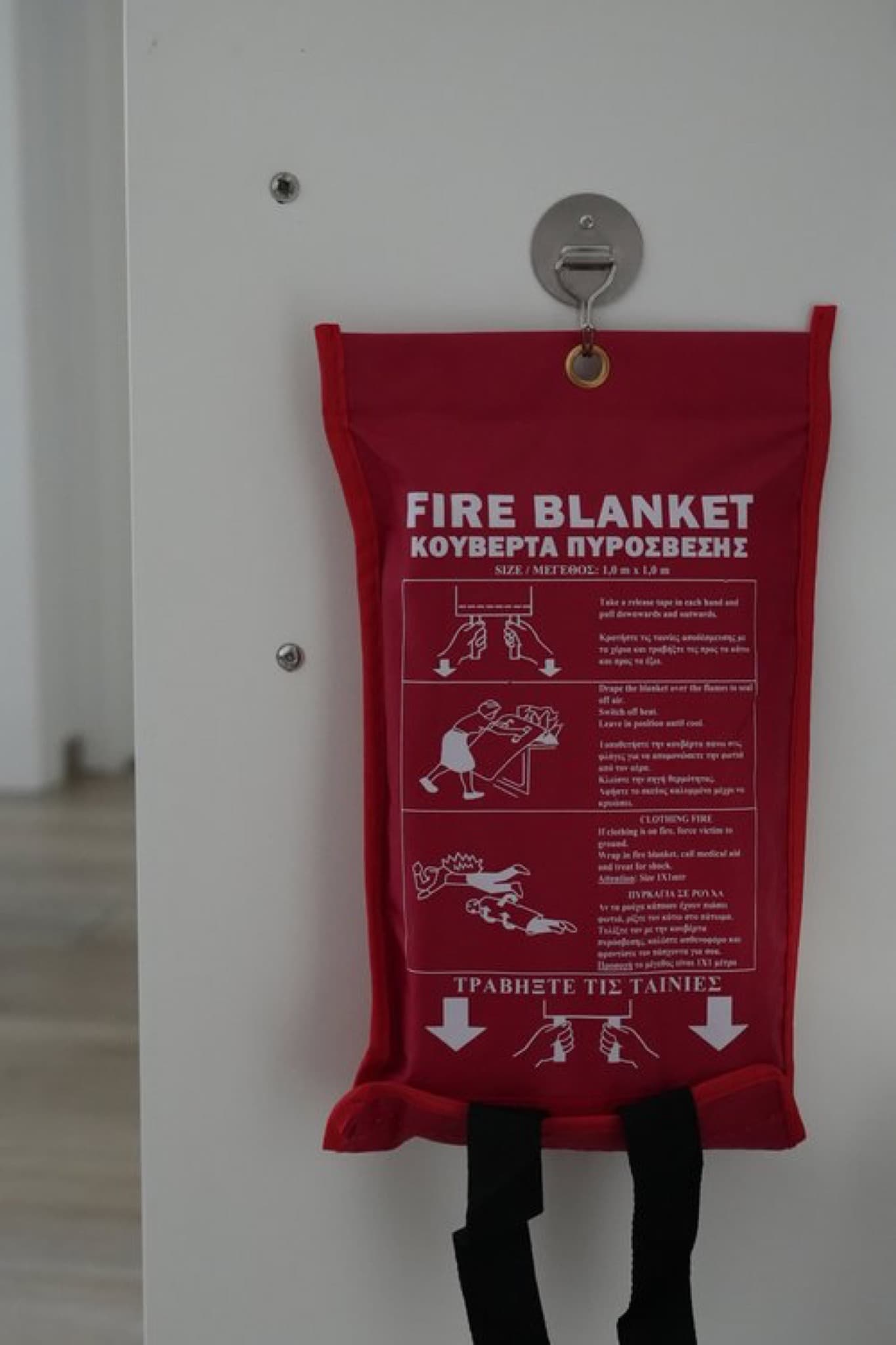 Red fire blanket pouch with bilingual pull instructions hung on white wall