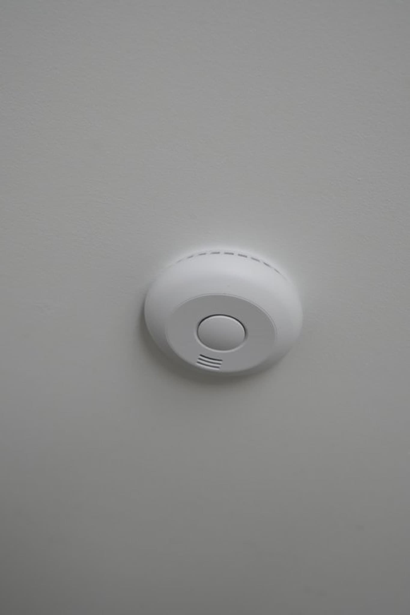 White dome smoke detector with central test button on grey ceiling