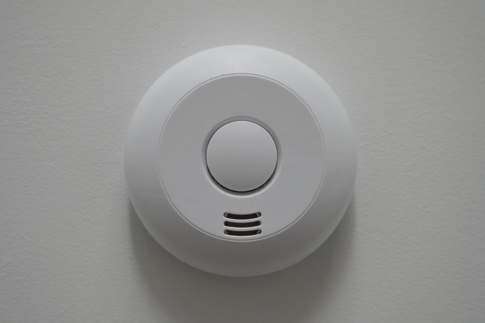 White round smoke detector with central button and three ventilation slots on white ceiling