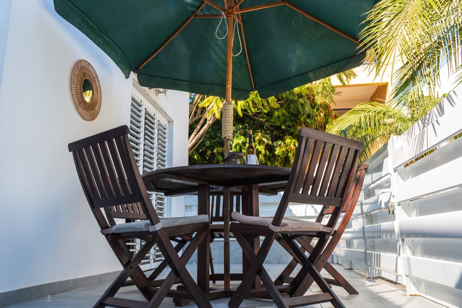 Palm-framed terrace with round dining table, four chairs, and wine glasses