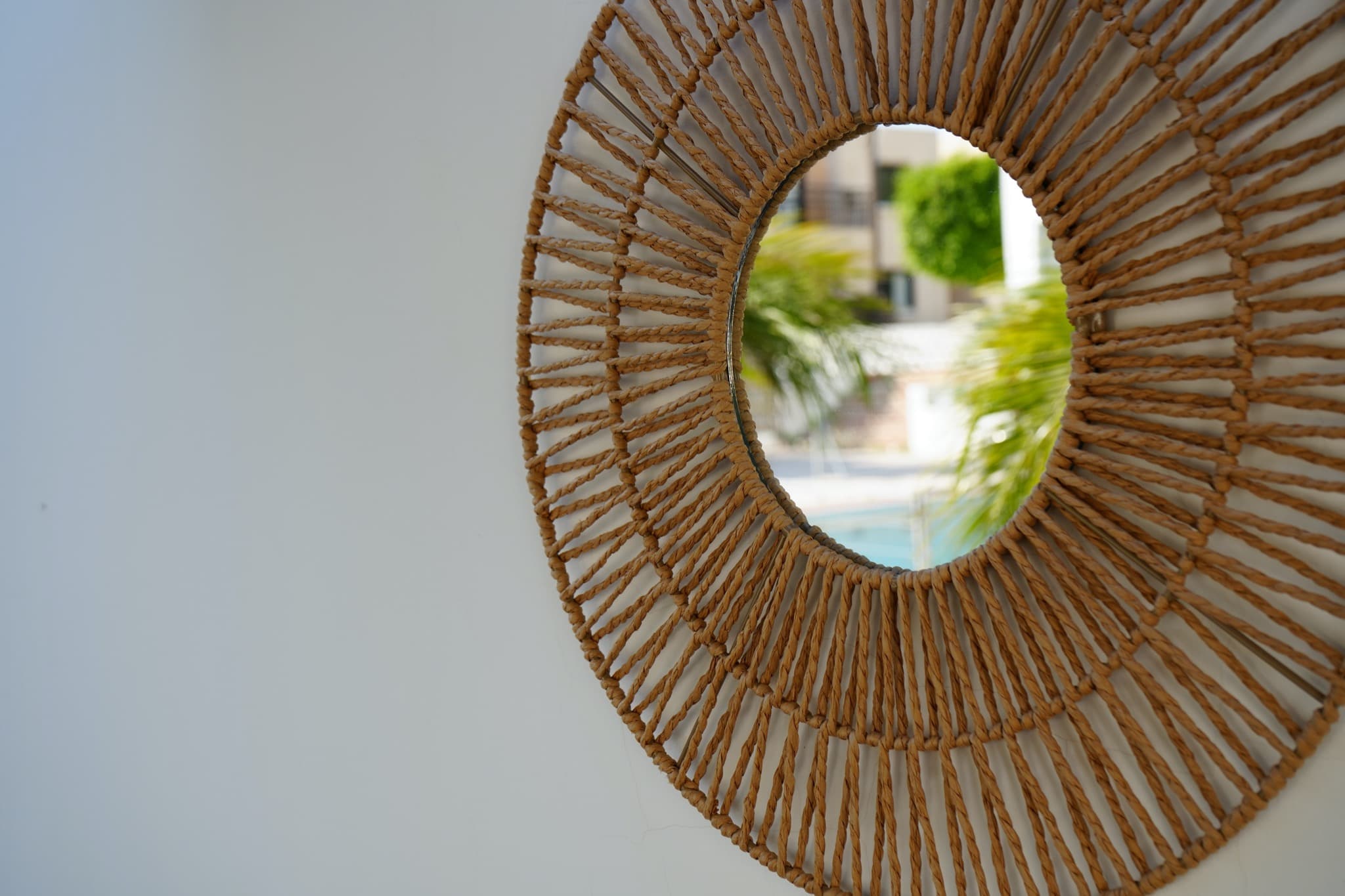 Rattan sunburst wall mirror reflecting palm leaves and courtyard