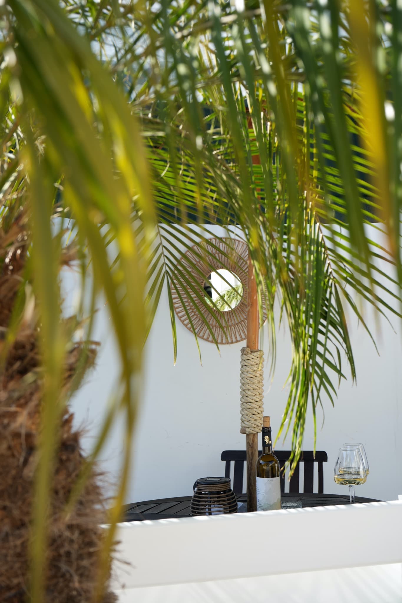 Patio table with wine bottle beneath palm fronds and rope-wrapped umbrella