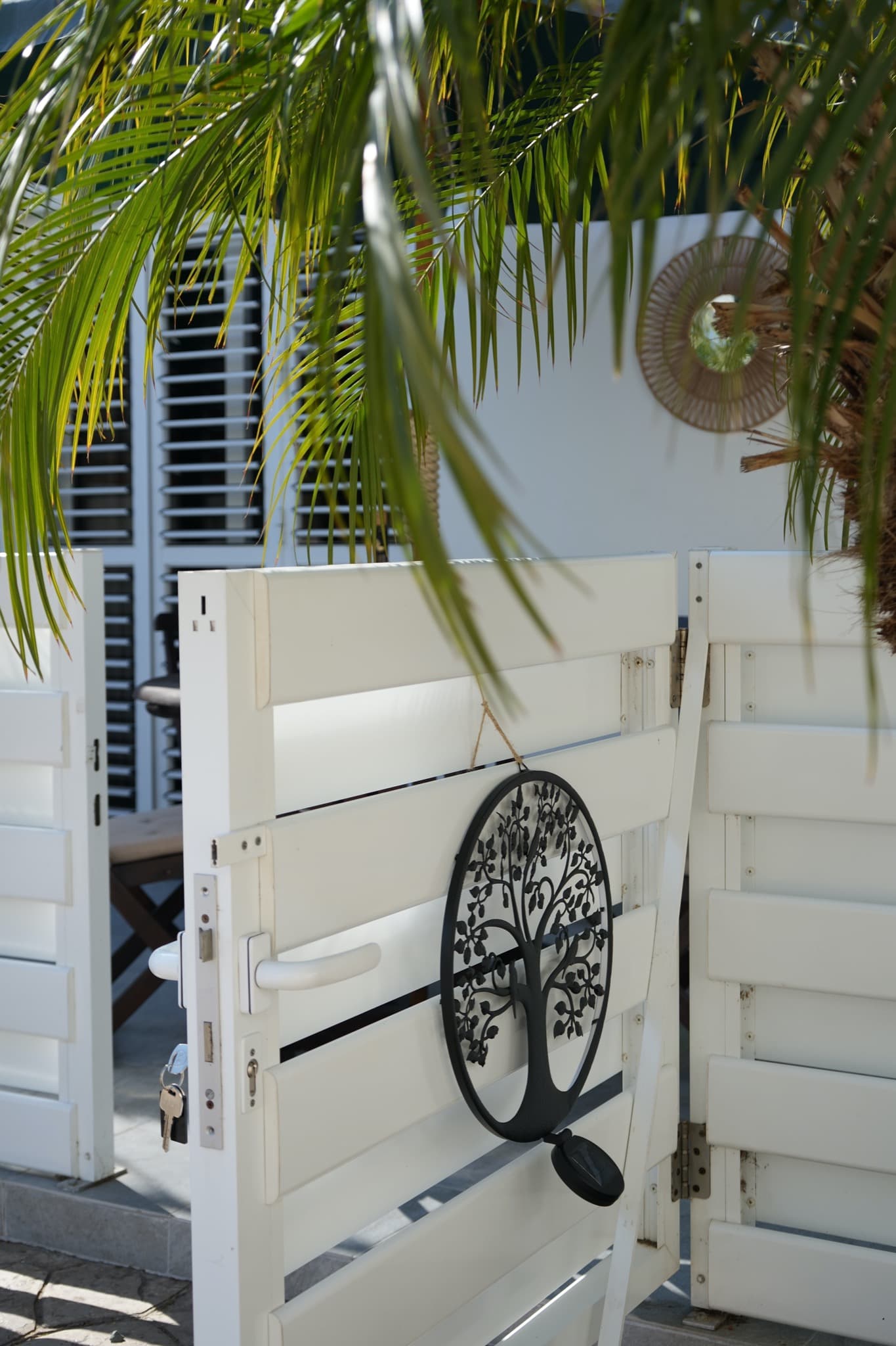 White slatted gate with black tree ornament and keys in lock
