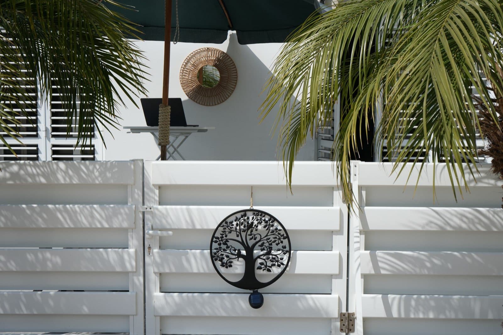 White slatted fence with black tree ornament, palm fronds, and umbrella