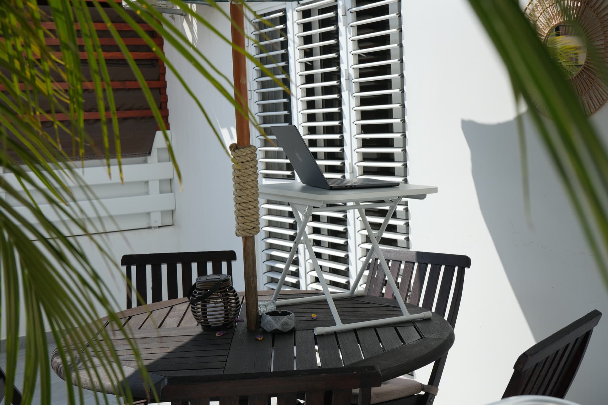 Round patio table with laptop stand, ashtray, and shuttered windows