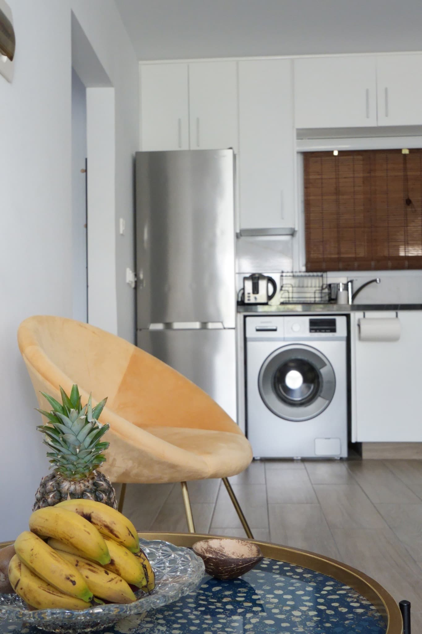 Glass coffee table with bananas and pineapple before yellow chair and kitchenette