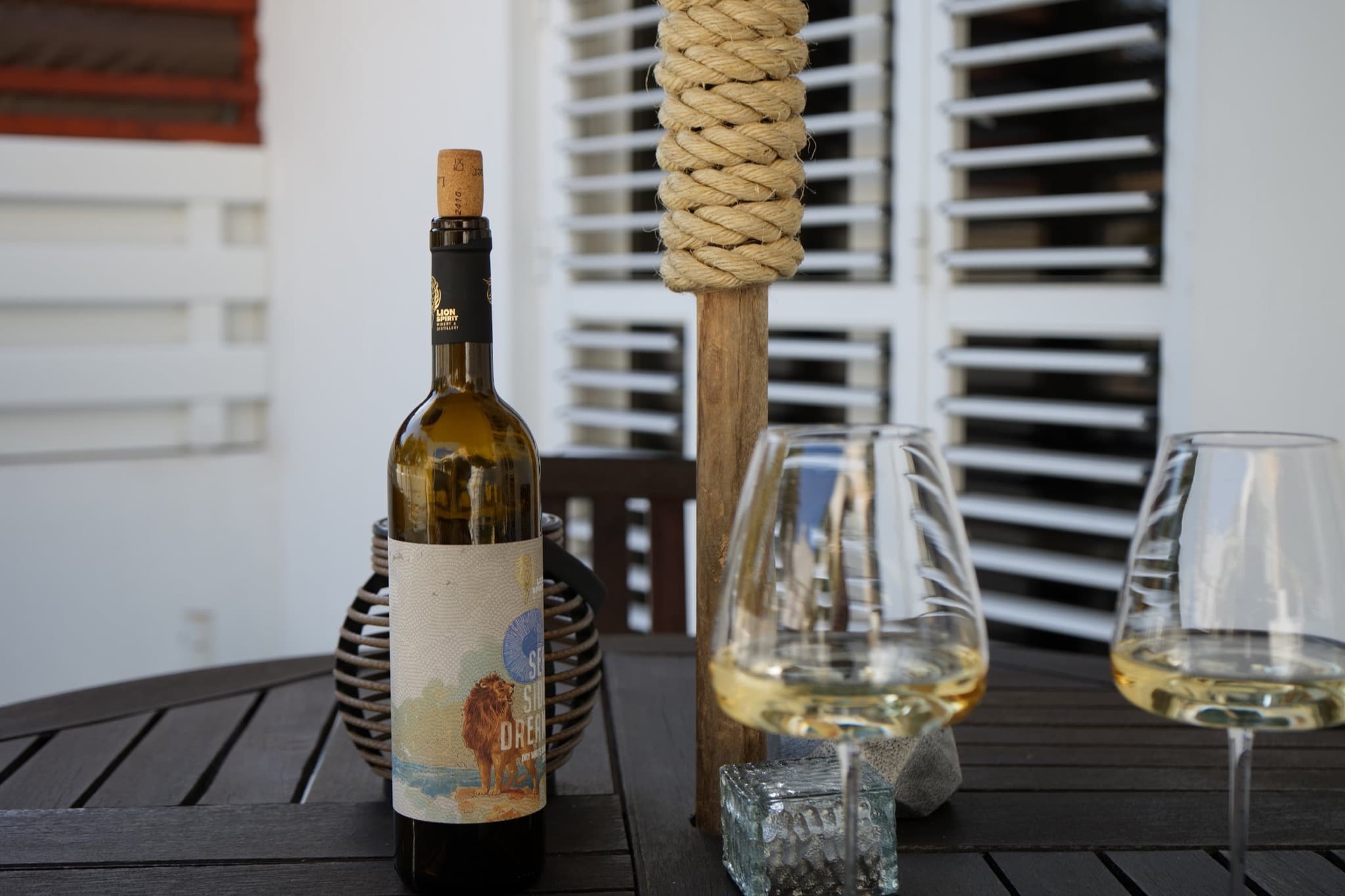 Wine bottle, two stemless glasses, and rope umbrella base on black patio table