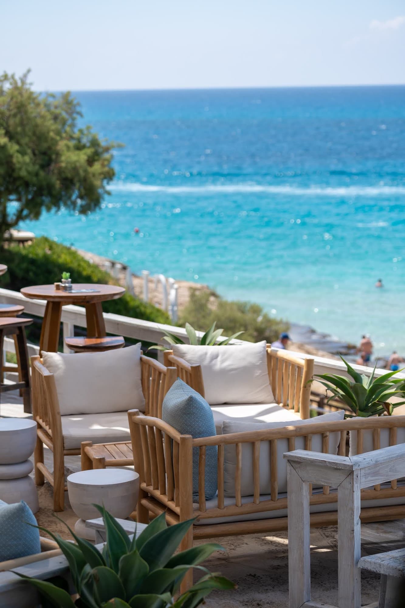 Teak outdoor sofa with white cushions on cliff-top restaurant terrace above turquoise sea