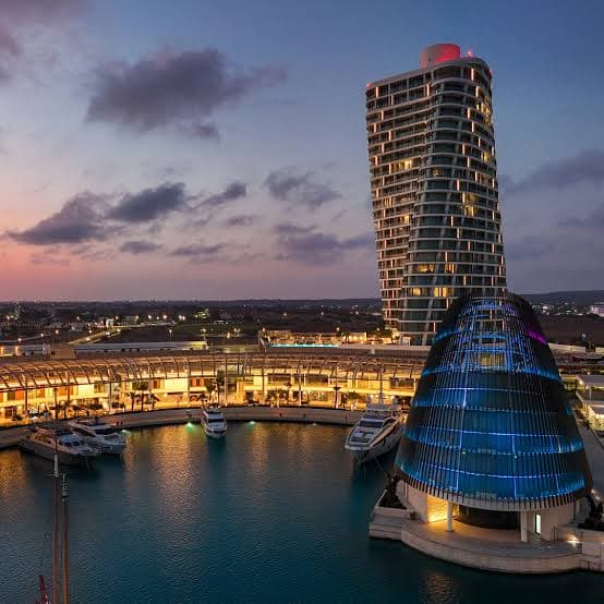 Aerial dusk view of Ayia Napa Marina's yacht basin and glass-domed building beneath the residential tower