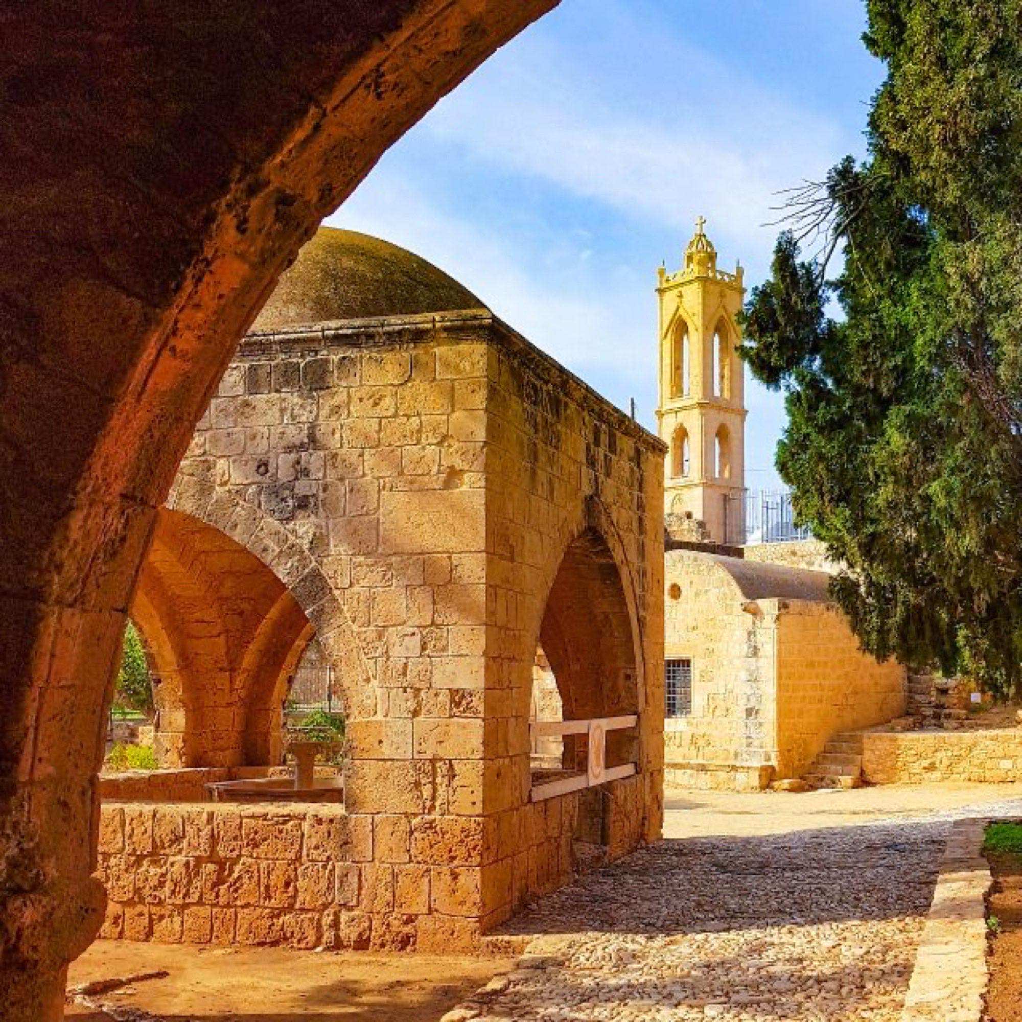 Stone archway framing the monastery's domed roof and bell tower among cypress trees