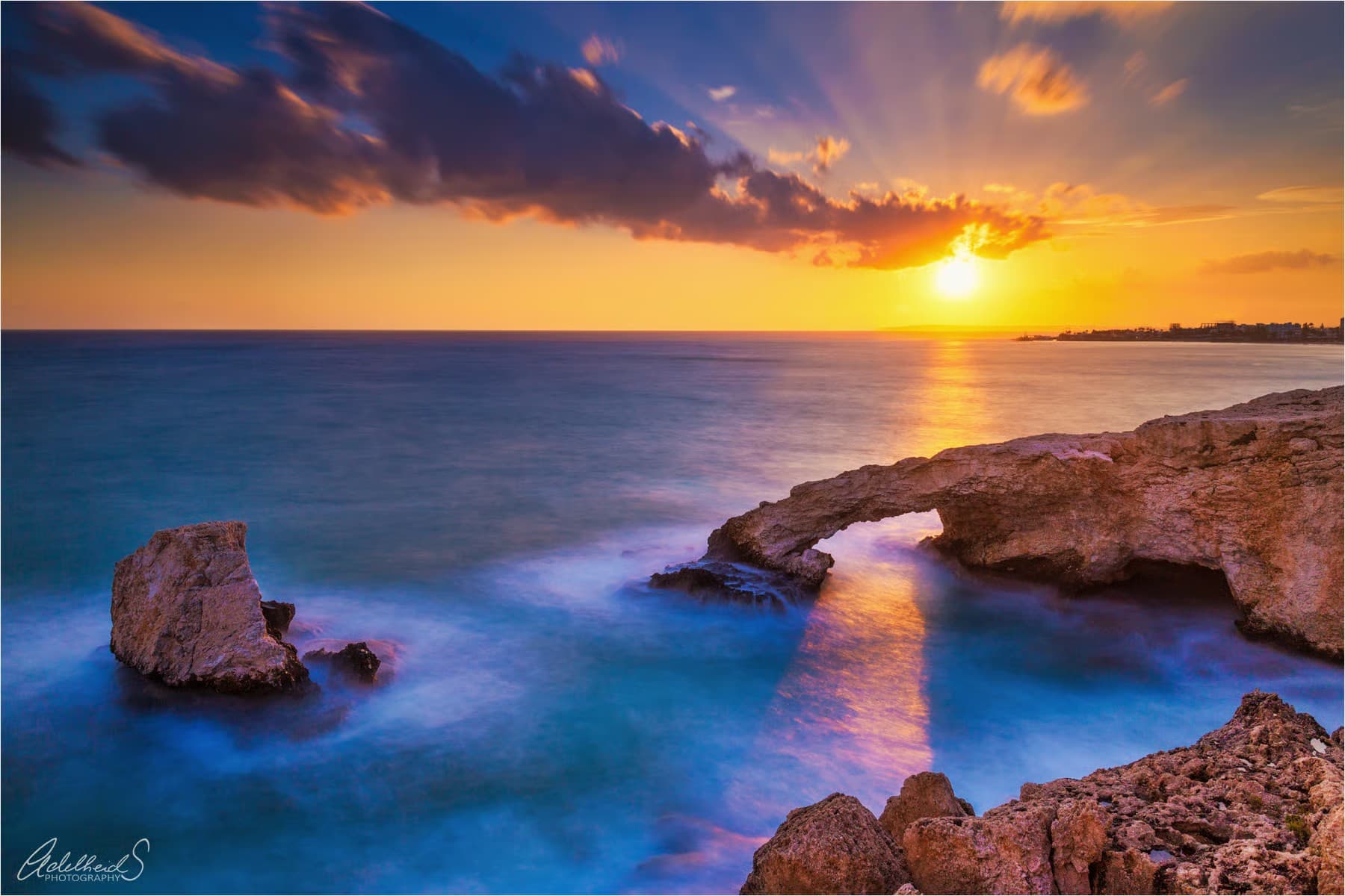 Natural limestone sea arch over turquoise water at sunset