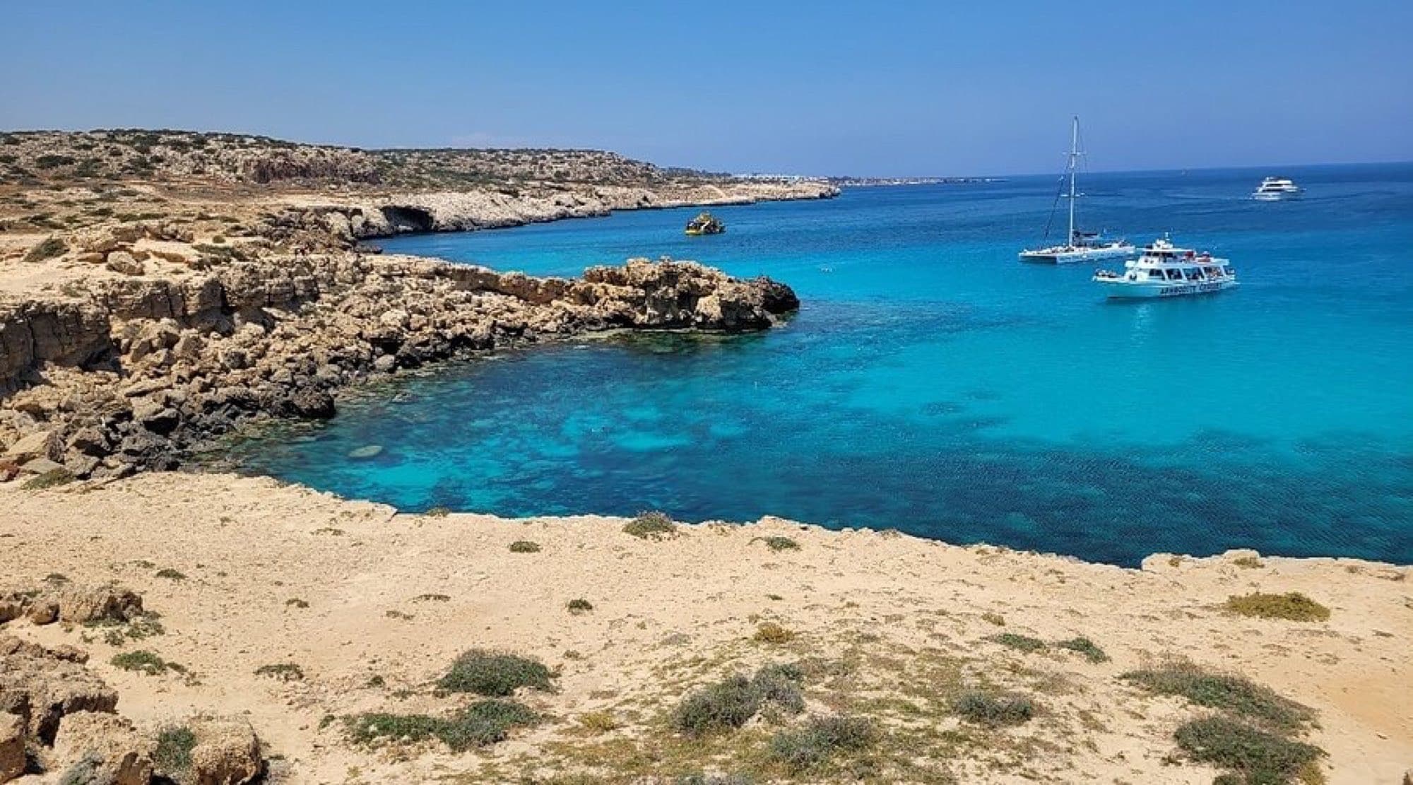 Turquoise lagoon and rocky headland at Cape Greco with tour boats anchored offshore