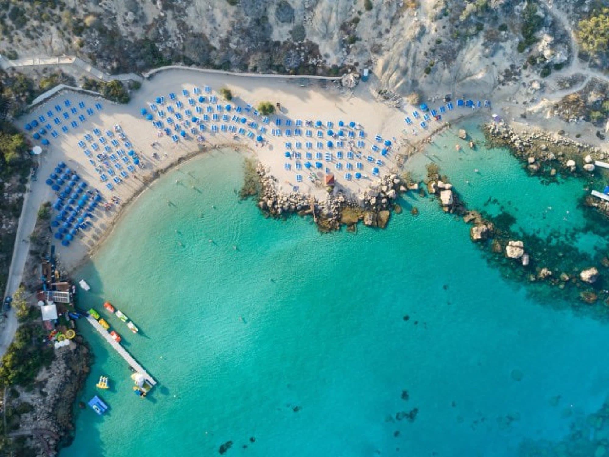 Aerial view of Konnos Bay's sheltered cove with sunbeds lining the sandy shore