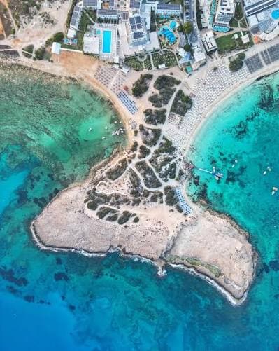 Aerial view of Makronissos Beach's sandy headland between two turquoise coves