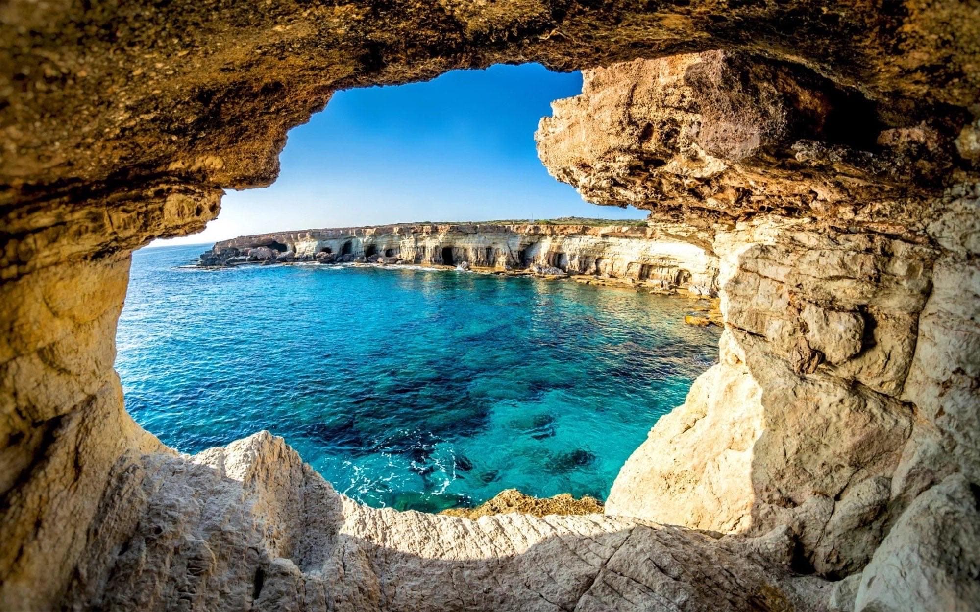 View through a sea cave arch out to the limestone cliffs and blue water of Cape Greco